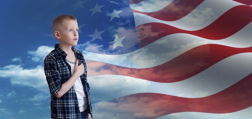 Niño patriótico orgulloso con la mano en su corazón mirando la bandera americana. | Fuente: Shutterstock