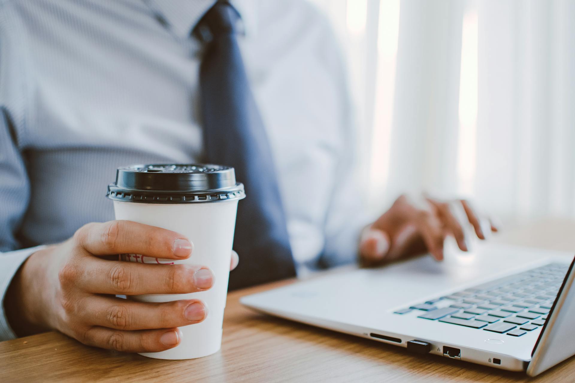 Primer plano de un hombre trabajando en su portátil mientras sostiene su taza de café | Fuente: Pexels