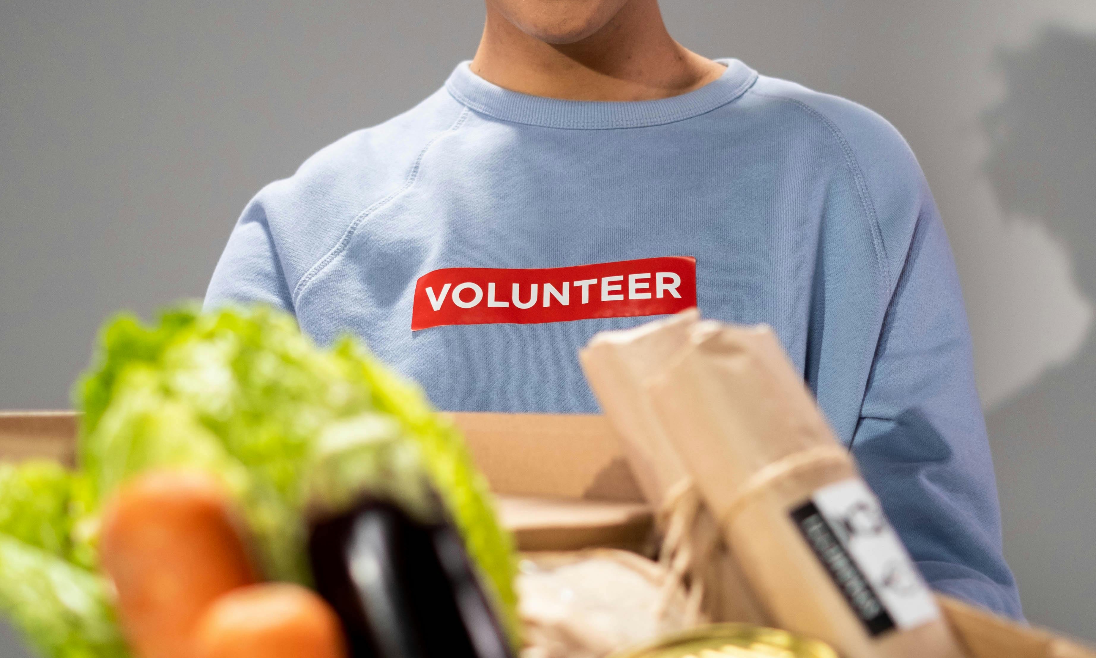 Una mujer con una camiseta estampada de "voluntaria" sosteniendo un paquete de comida | Fuente: Pexels