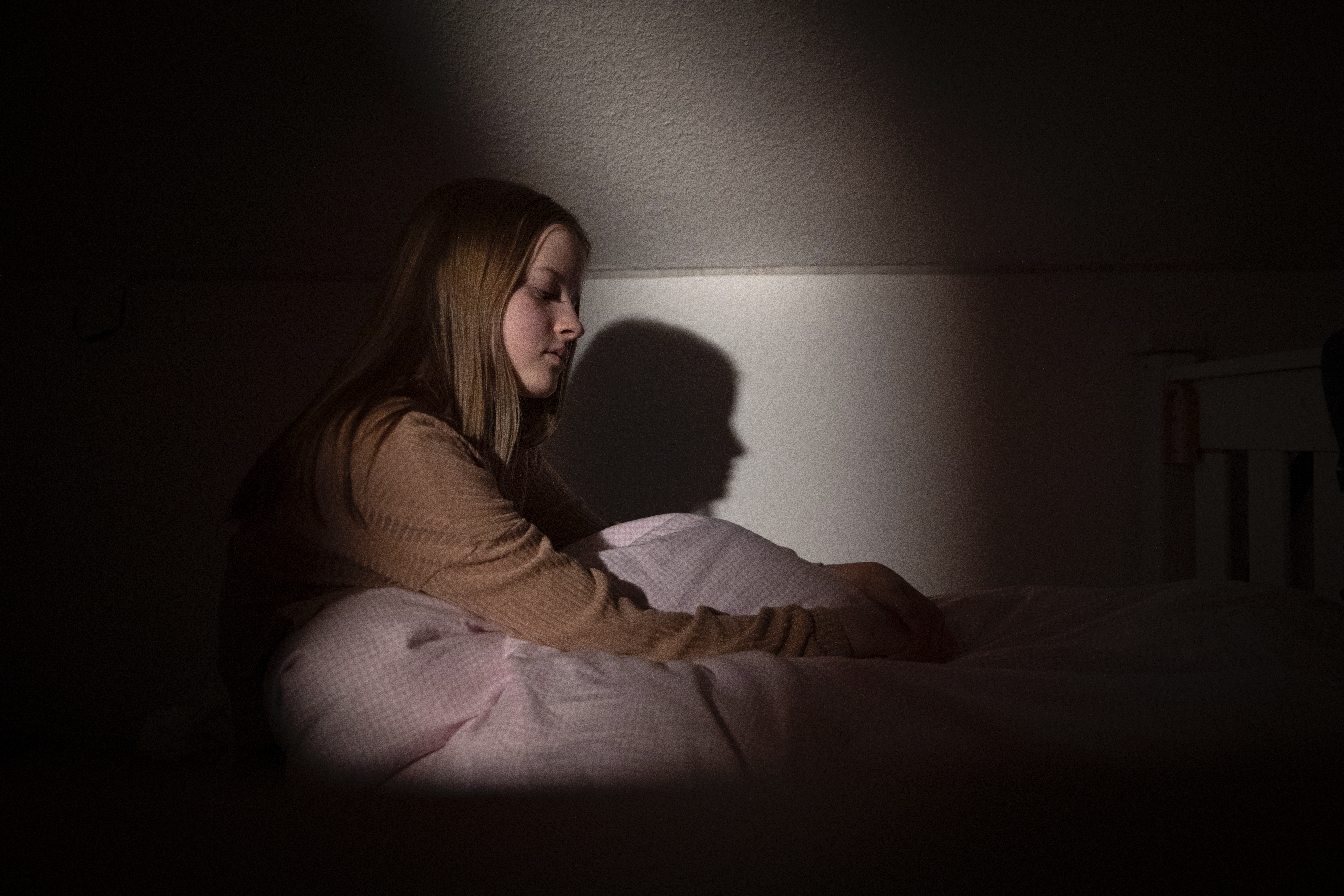 Adolescente sentada en la cama por la noche con poca luz y expresión facial que representa desesperación y tristeza | Foto: Getty Images