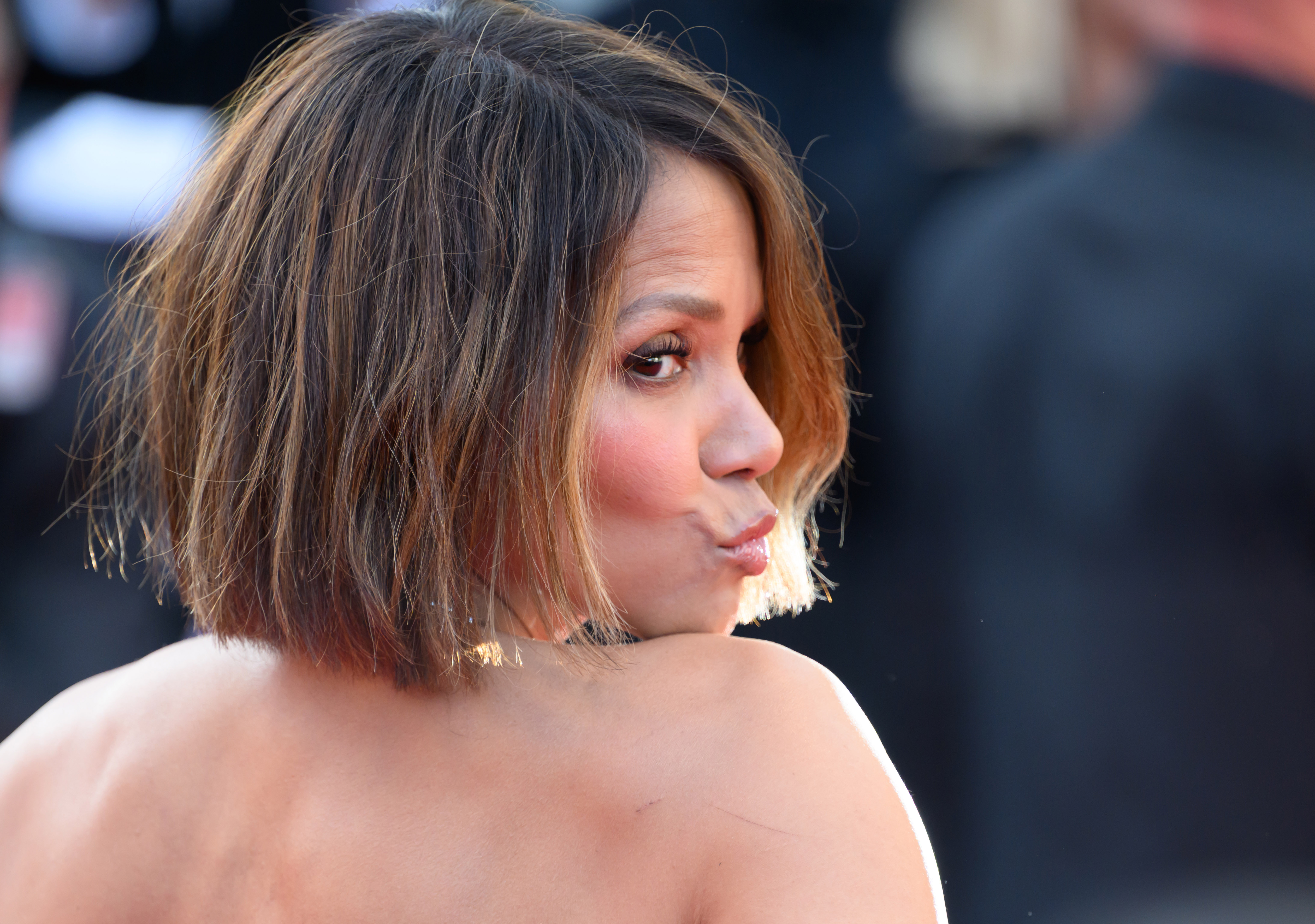 Halle Berry frunce los labios en una pose juguetona, mirando hacia atrás por encima del hombro con una expresión pícara mientras habla con las cámaras en la alfombra roja.