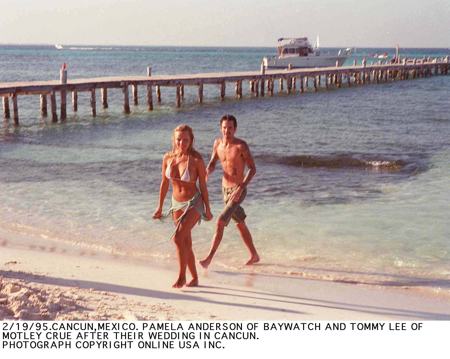 Los recién casados Pamela Anderson y Tommy Lee, el batería de Mötley Crüe, pasean descalzos por la soleada playa de Cancún, México, solo unos días después de su boda relámpago en febrero de 1995. Con un bikini blanco y un pareo atado, junto a Lee, que lleva unos pantalones cortos de surf, este momento tan mediático en la playa marca la intensa tormenta mediática que acompañó los inicios de la fama de Anderson: un capítulo caótico que, con el tiempo, la llevaría a buscar refugio en la tranquilidad y la soledad de la isla de Vancouver. | Fuente: Getty Images