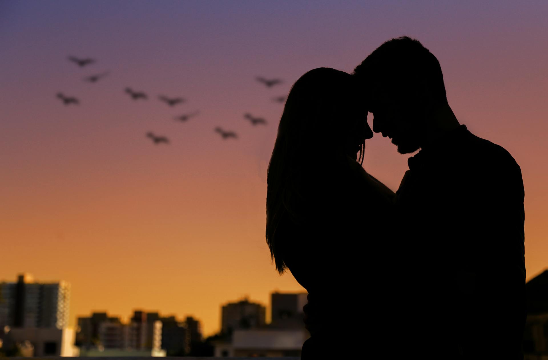 Una pareja silueteada contra el horizonte de una ciudad al atardecer | Fuente: Pexels