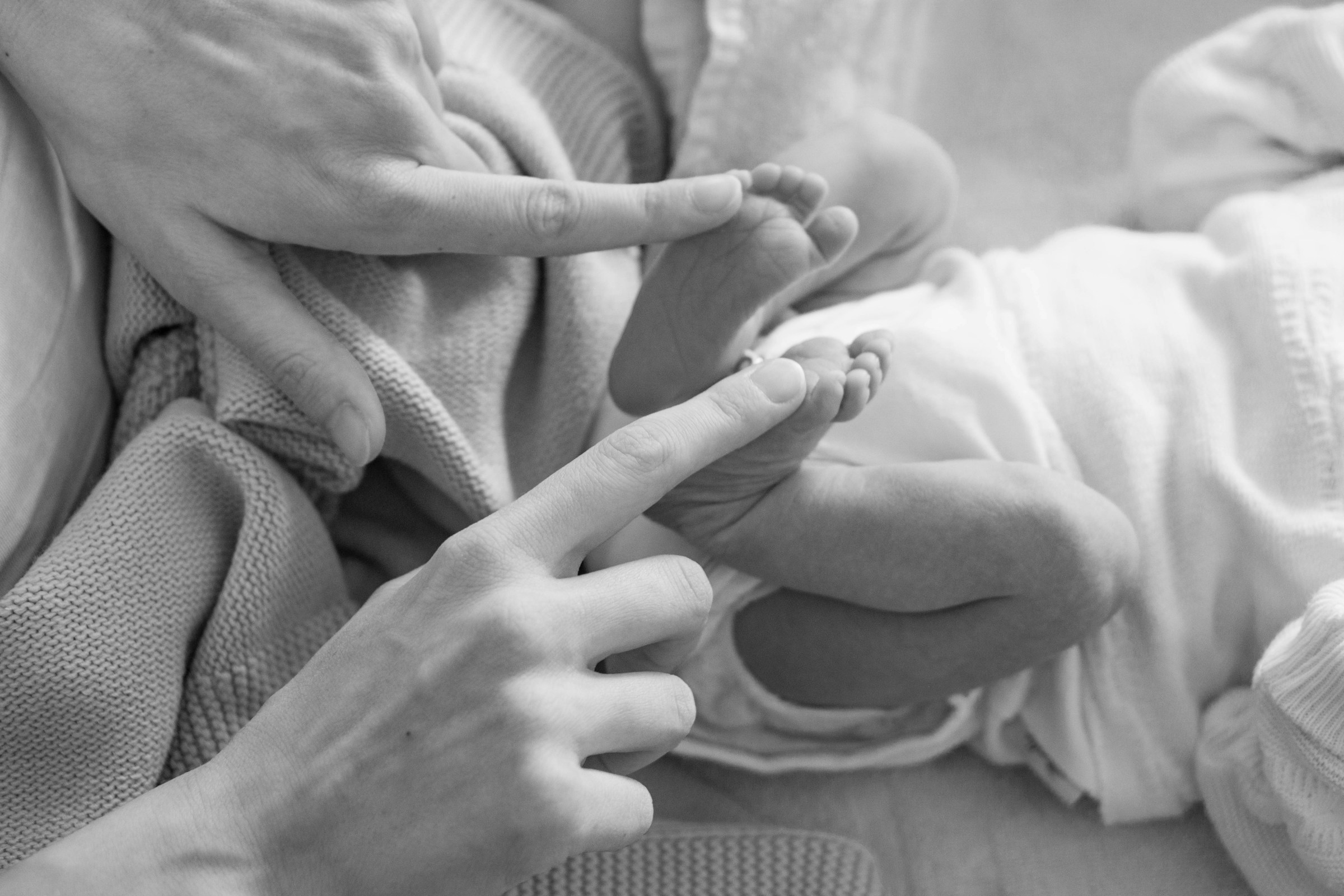 Foto en escala de grises de una madre tocando los piececitos de su bebé recién nacido | Fuente: Unsplash