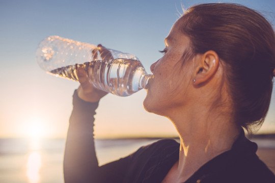 Mujer tomando agua de una botellas de plástico | Foto: Getty Images
