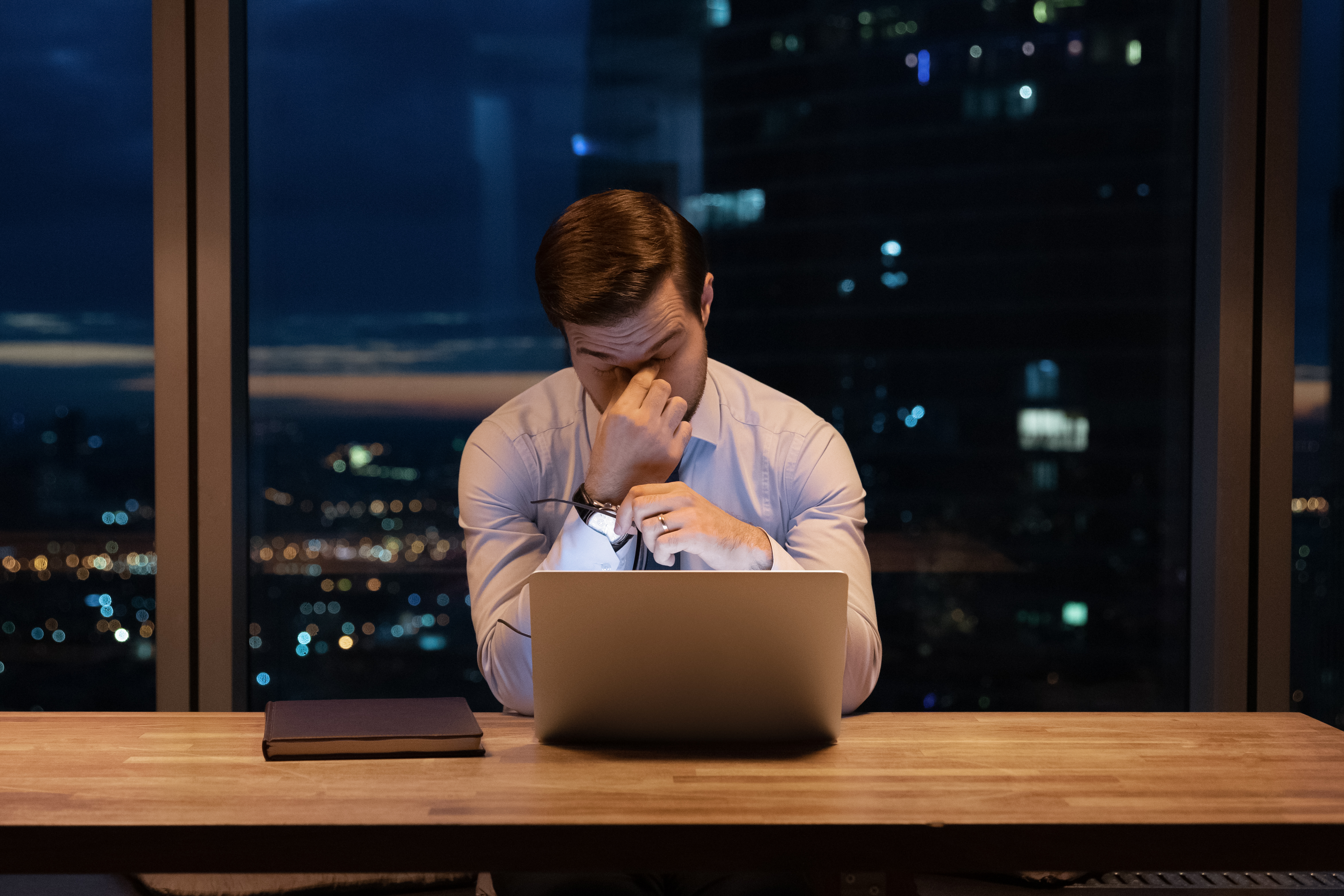 Un hombre con exceso de trabajo se siente cansado mientras trabaja con su portátil por la noche | Fuente: Shutterstock