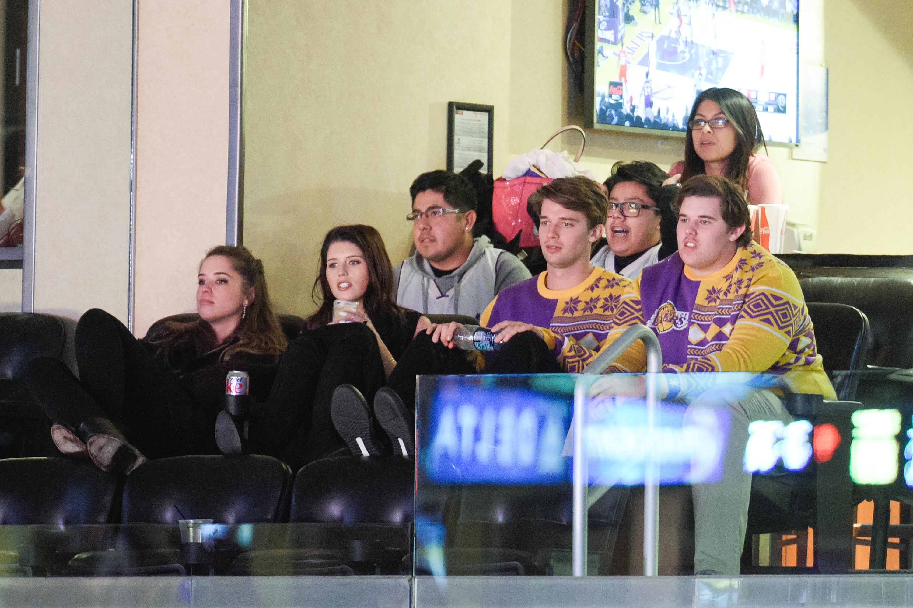 En otro momento del mismo partido, Christopher está sentado junto a sus hermanos, Christina, Katherine y Patrick. Concentrado en la acción, se mezcla con la multitud festiva, su jersey con motivos navideños hace juego con el de Patrick mientras se inclina hacia delante con visible energía y atención.