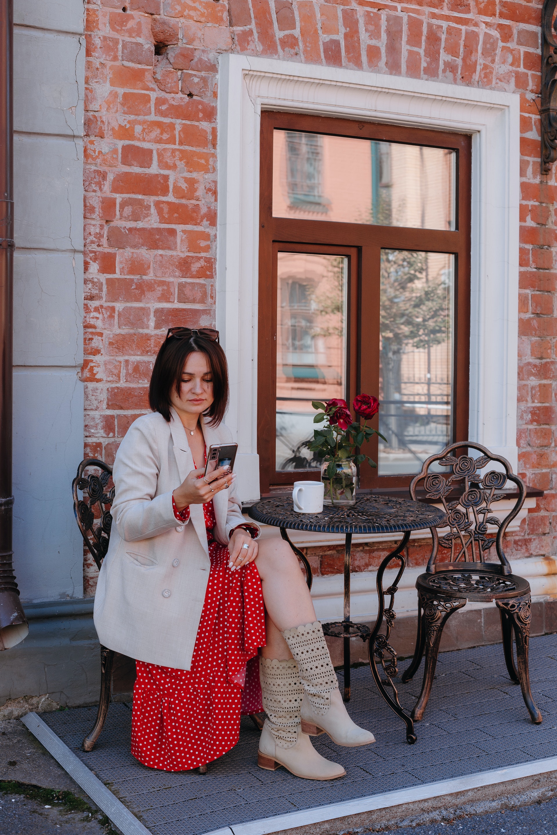 Una mujer sentada en una cafetería de la acera mientras consulta su teléfono móvil. | Foto: Pexels