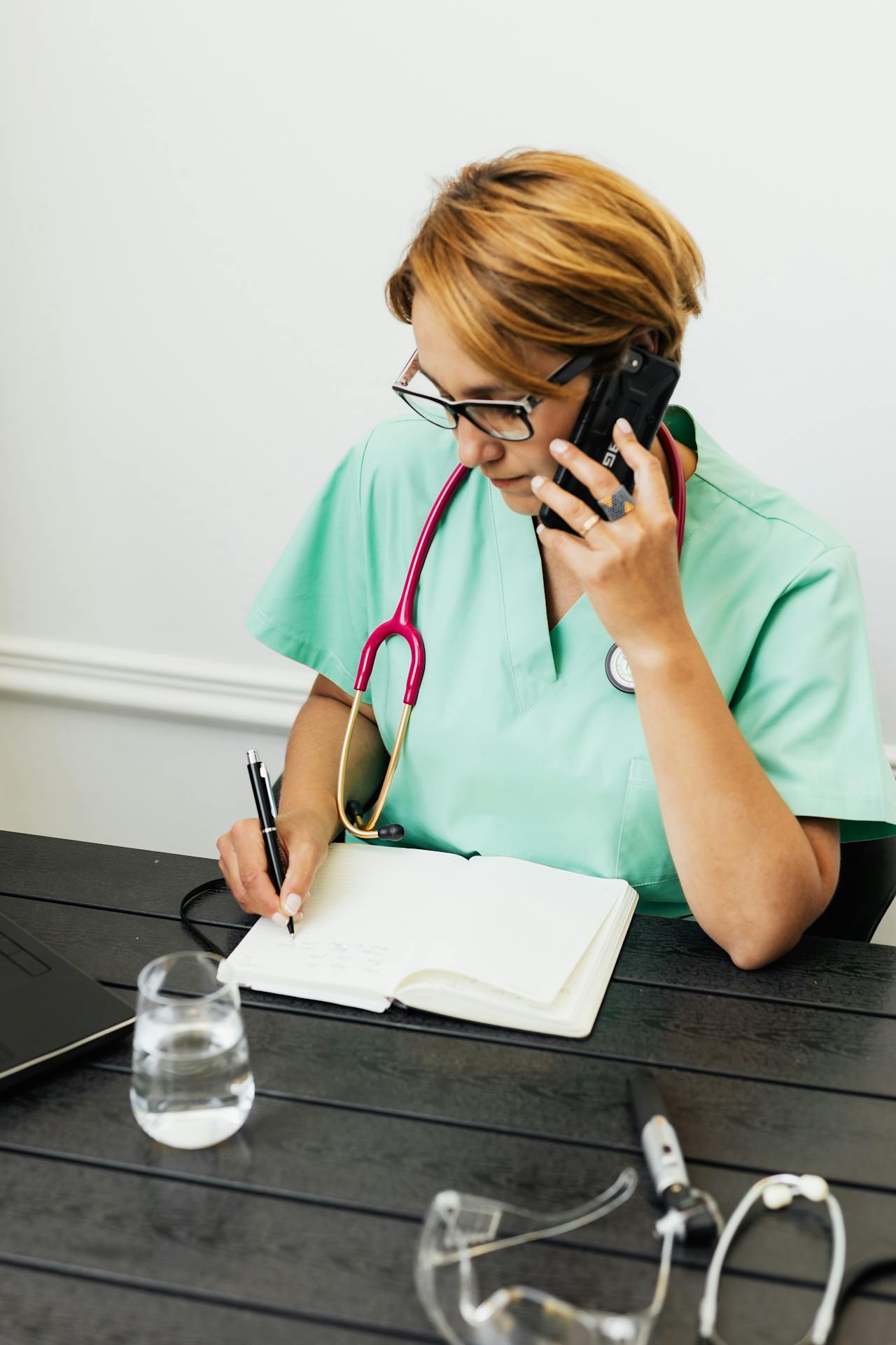 Personal médico hablando por teléfono mientras escribe en un cuaderno | Fuente: Pexels