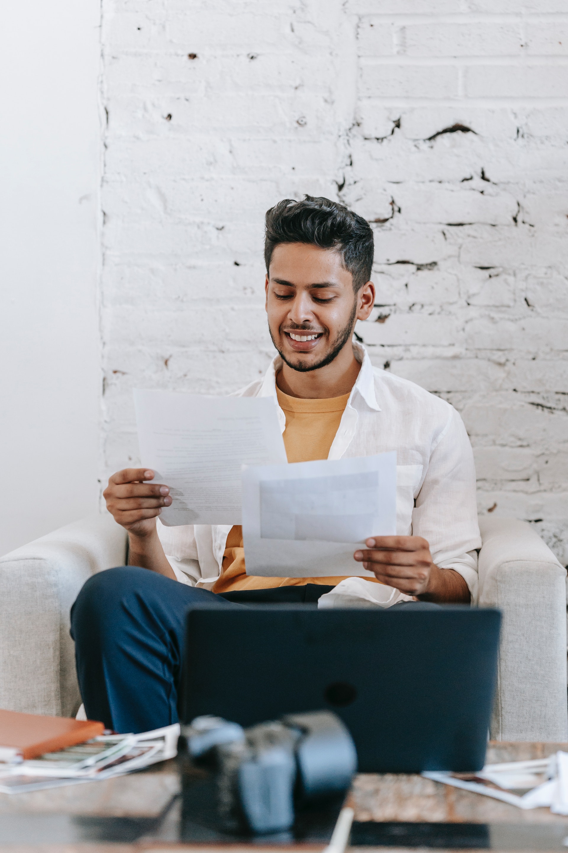 Un joven leyendo documentos y trabajando en un portátil | Fuente: Pexels