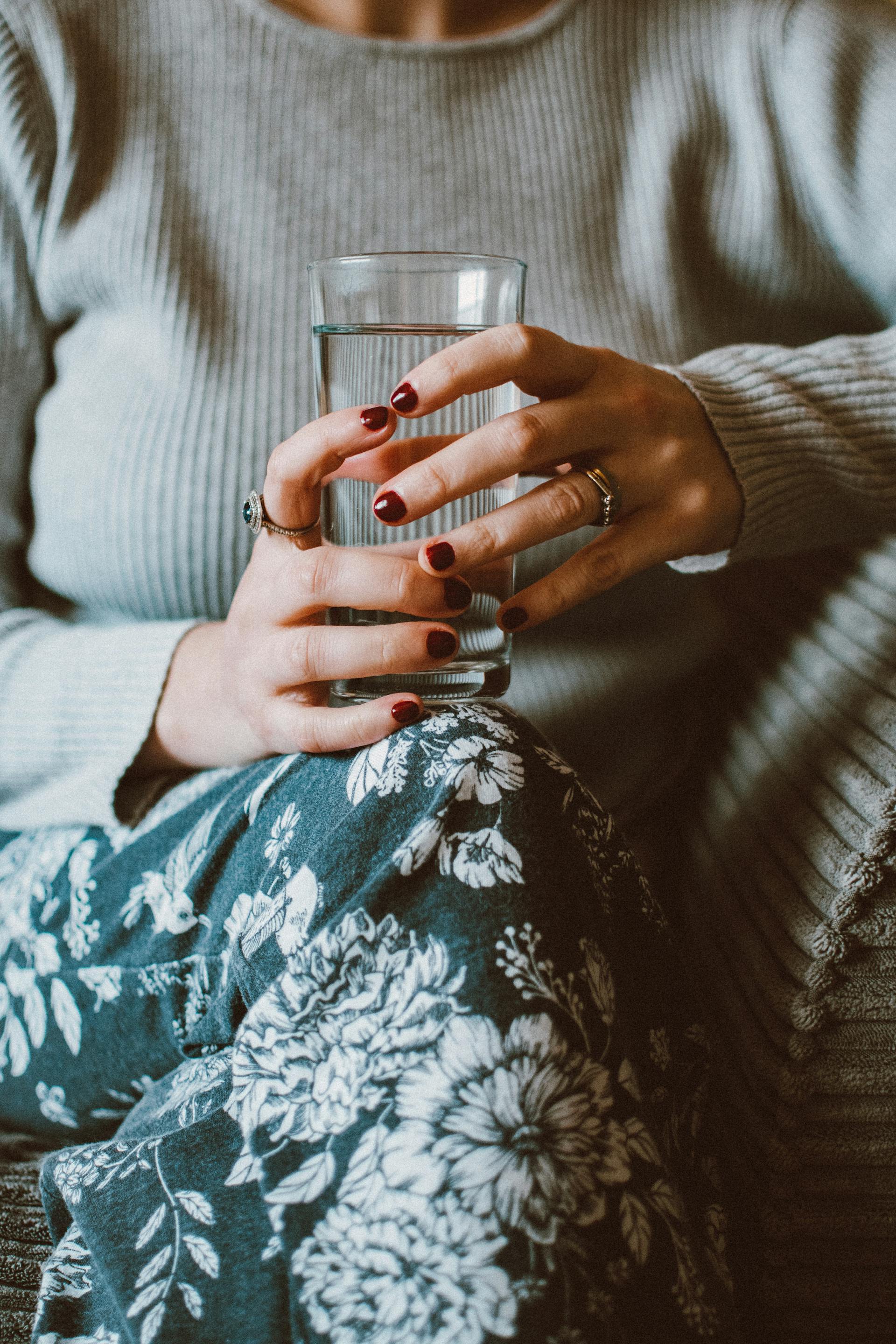 Una mujer sentada en un sofá mientras sostiene un vaso de agua | Fuente: Pexels