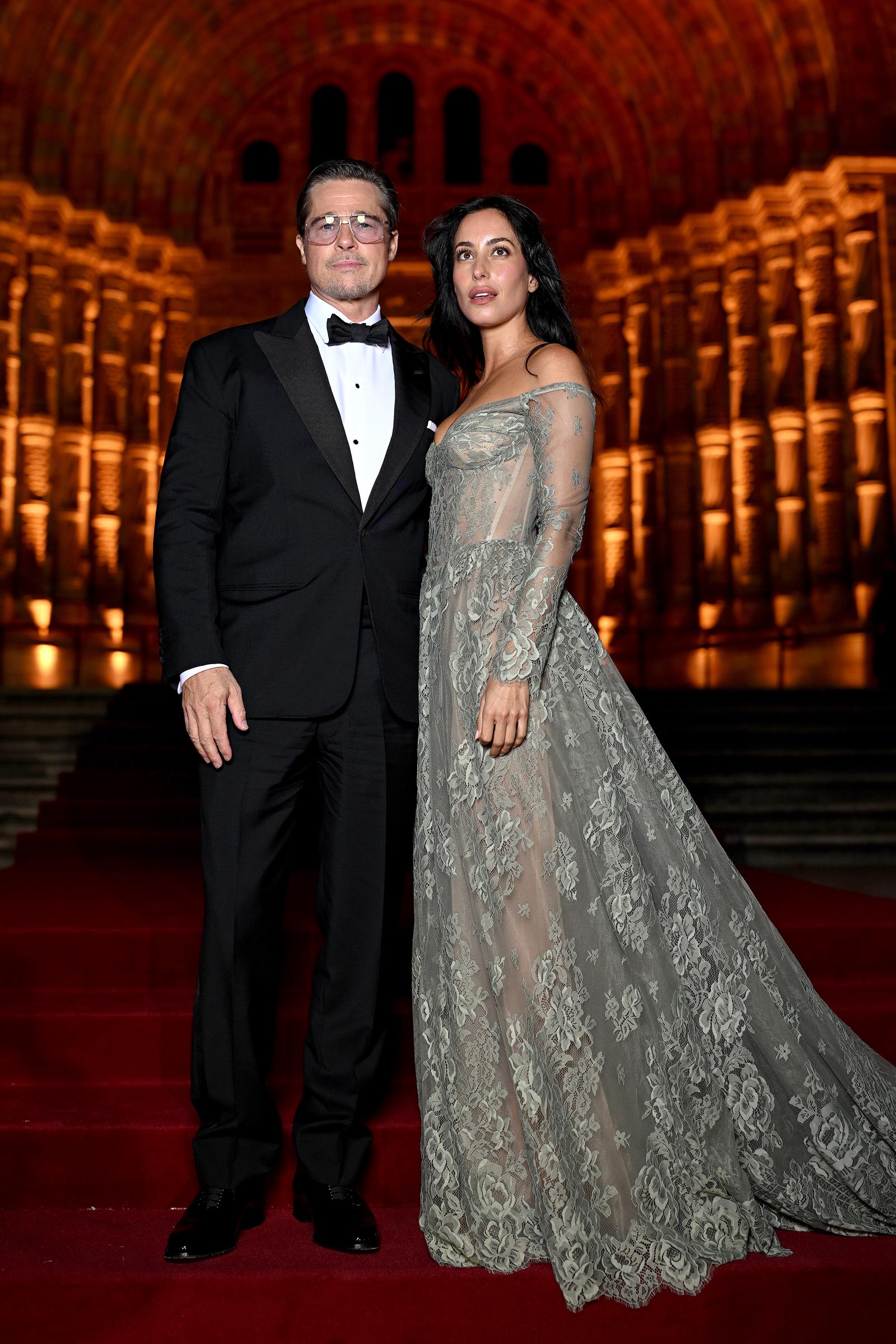Brad Pitt e Inés de Ramón posan para una foto de cuerpo entero en la escalera de la alfombra roja, luciendo sus contrastantes looks de gala. El vestido largo bordado de Inés tiene una cola espectacular que se despliega por los escalones, mientras que los resplandecientes arcos dorados del recinto crean un fondo impresionante. | Fuente: Getty Images