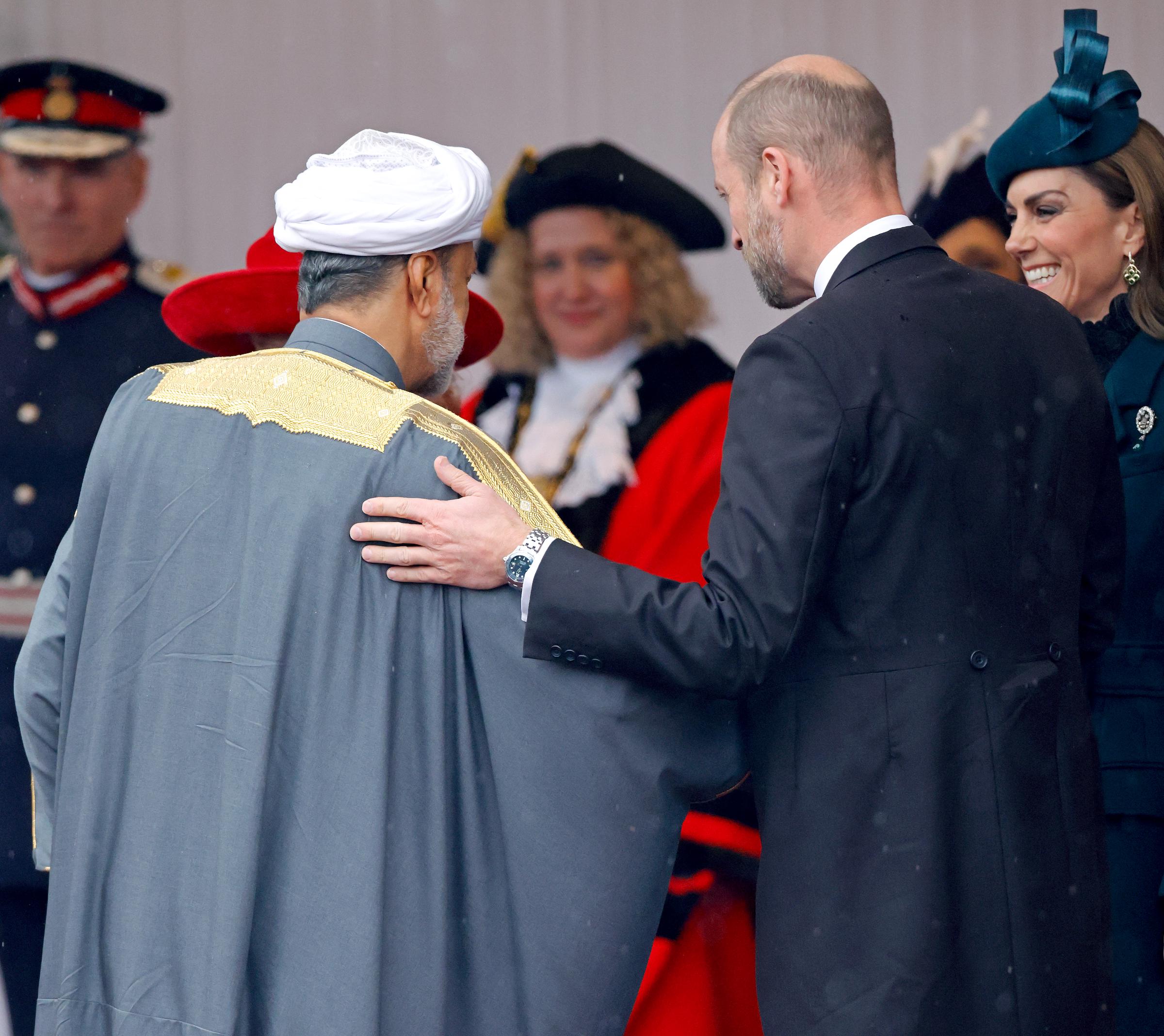 El príncipe William saluda cordialmente al sultán Haitham bin Tarik de Omán en la tribuna real de Datchet Road, Windsor, Inglaterra, el 20 de octubre de 2026, al inicio de su visita de Estado de tres días. De perfil y con chaqué oscuro, el príncipe de Gales posa una mano afectuosa sobre el hombro del sultán. Detrás, Catherine, princesa de Gales, sonríe con un tocado verde esmeralda hecho a medida por Juliette Millinery y un conjunto de encaje de cuello alto. | Fuente: Getty Images