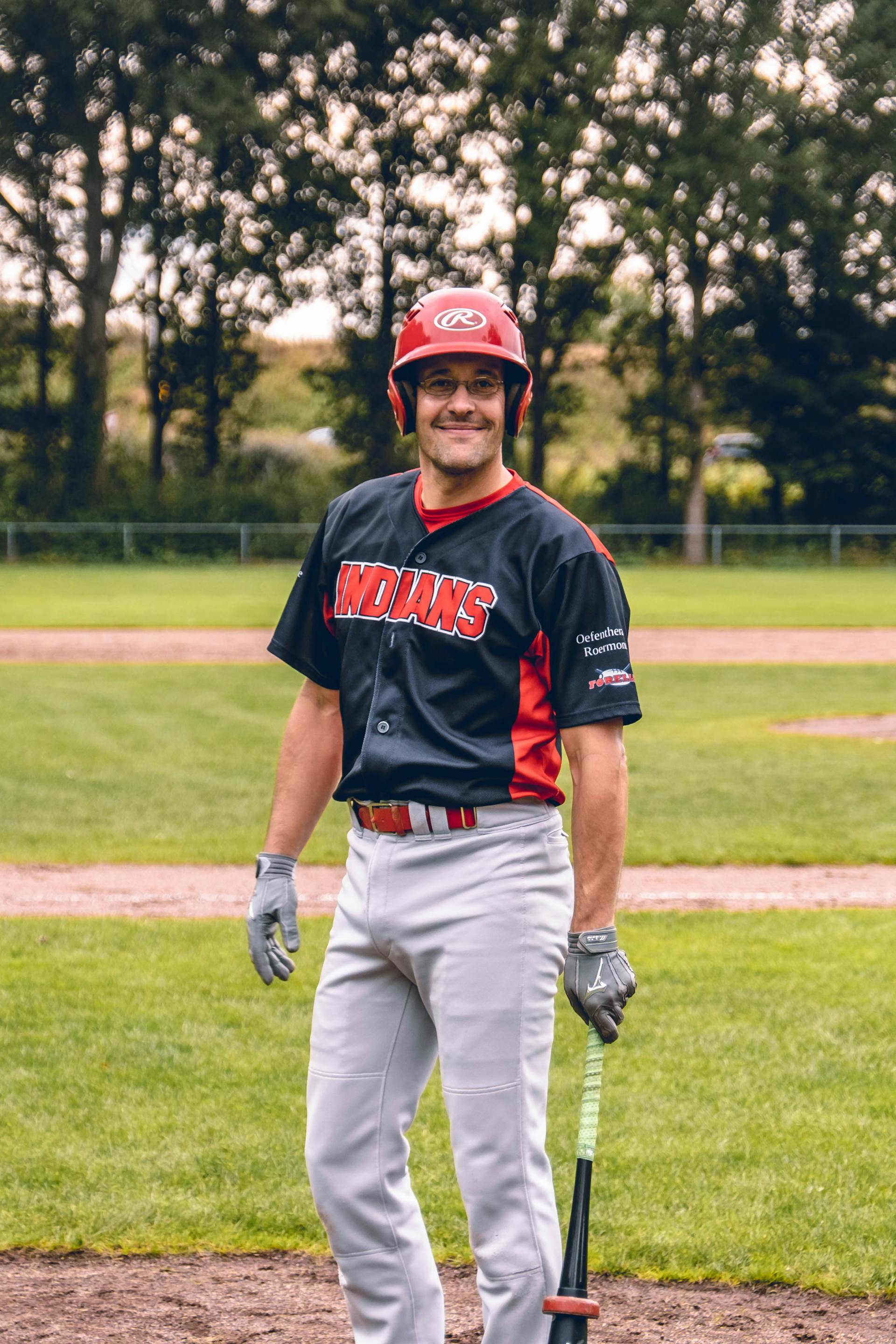 Un hombre con uniforme de béisbol de pie y sonriendo al aire libre | Fuente: Pexels