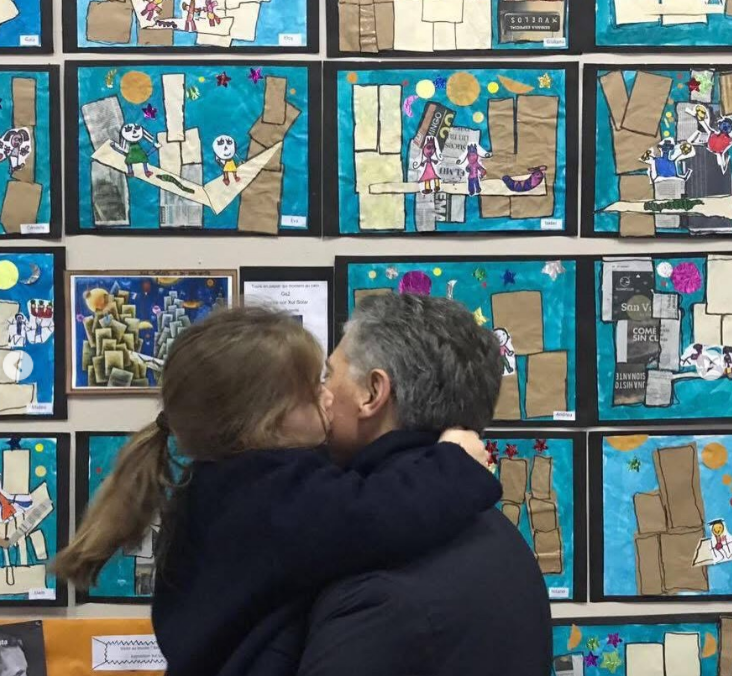 Mauricio Macri sostiene en brazos a Antonia frente a un colorido mural escolar repleto de collages y dibujos infantiles. La niña, con el pelo recogido en una coleta y abrigo oscuro, rodea el cuello de su padre con los brazos y le da un beso en la mejilla. | Fuente: Instagram/mauriciomacri