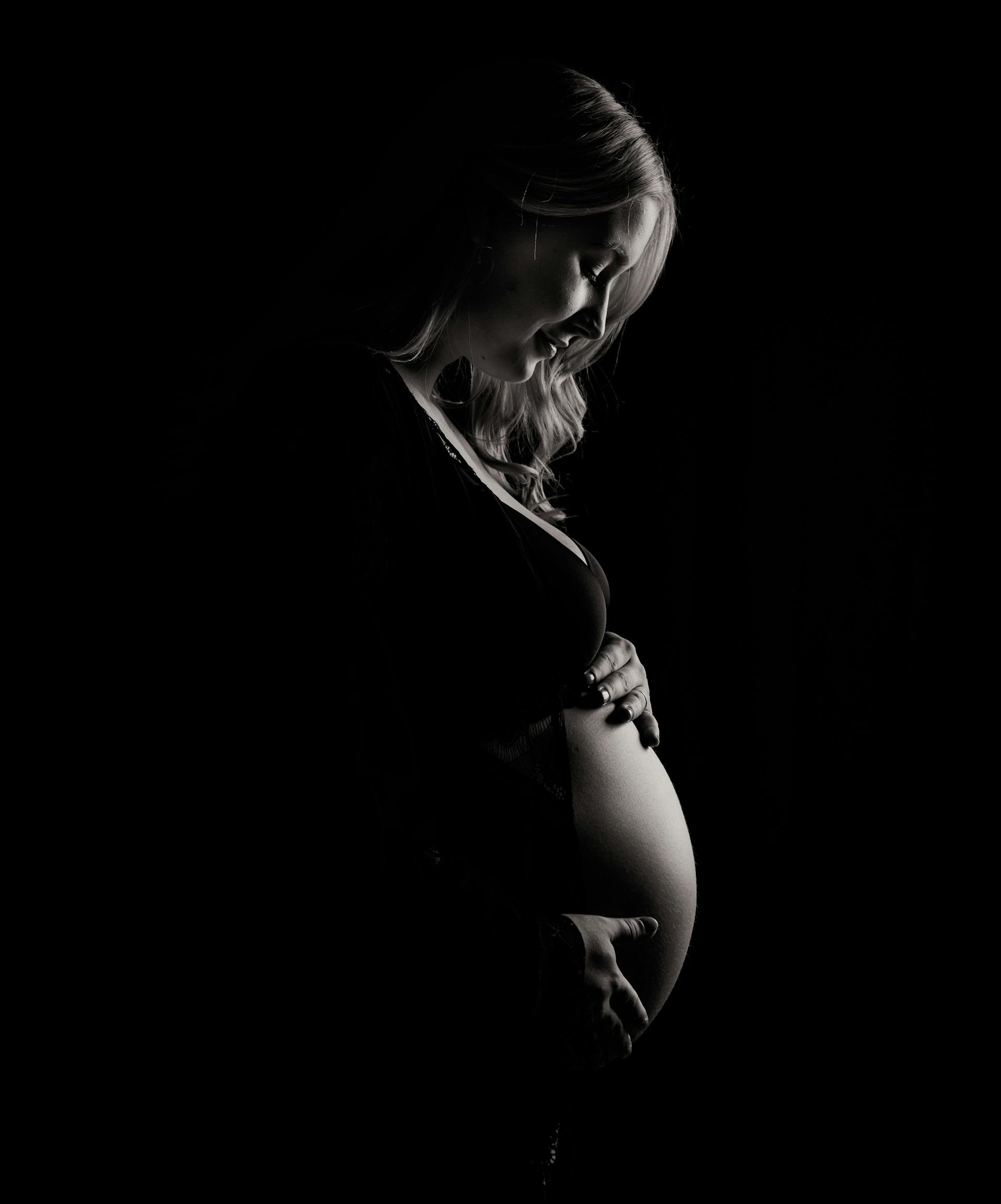 Foto en escala de grises de una mujer embarazada sujetando su barriguita | Fuente: Pexels