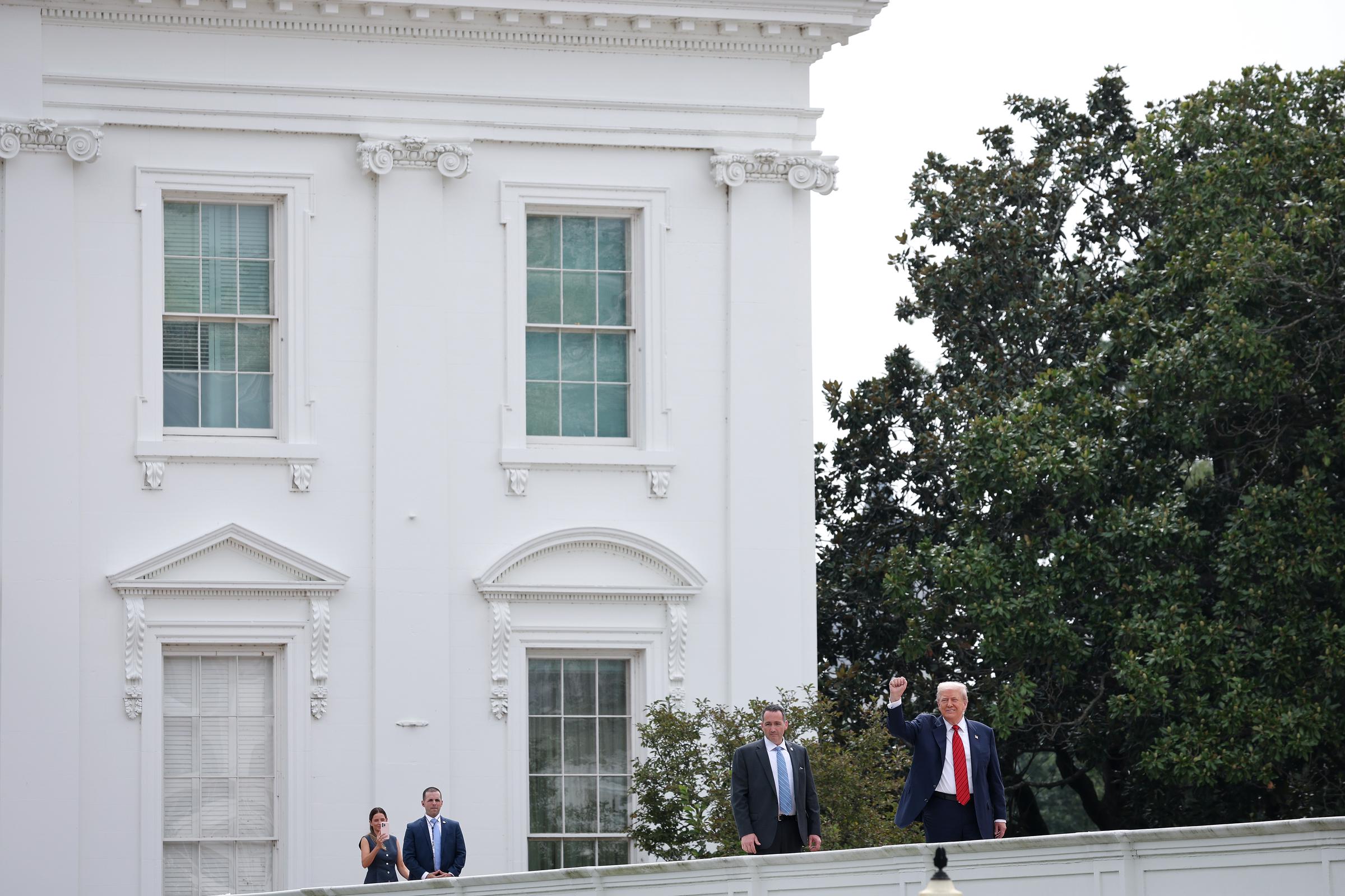 Donald Trump parece saludar mientras habla con los periodistas durante un recorrido por la azotea del ala oeste de la Casa Blanca en Washington, D.C., acompañado por ayudantes y personal de seguridad.
