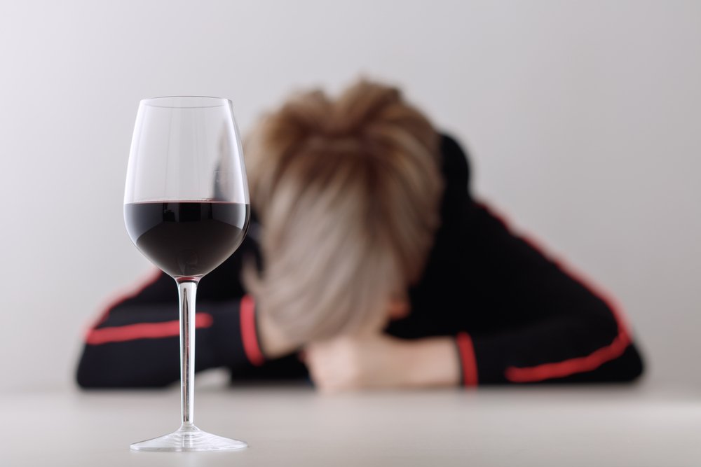 Mujer acostada sobre una mesa donde esta una copa con alcohol. | Foto: Shutterstock.