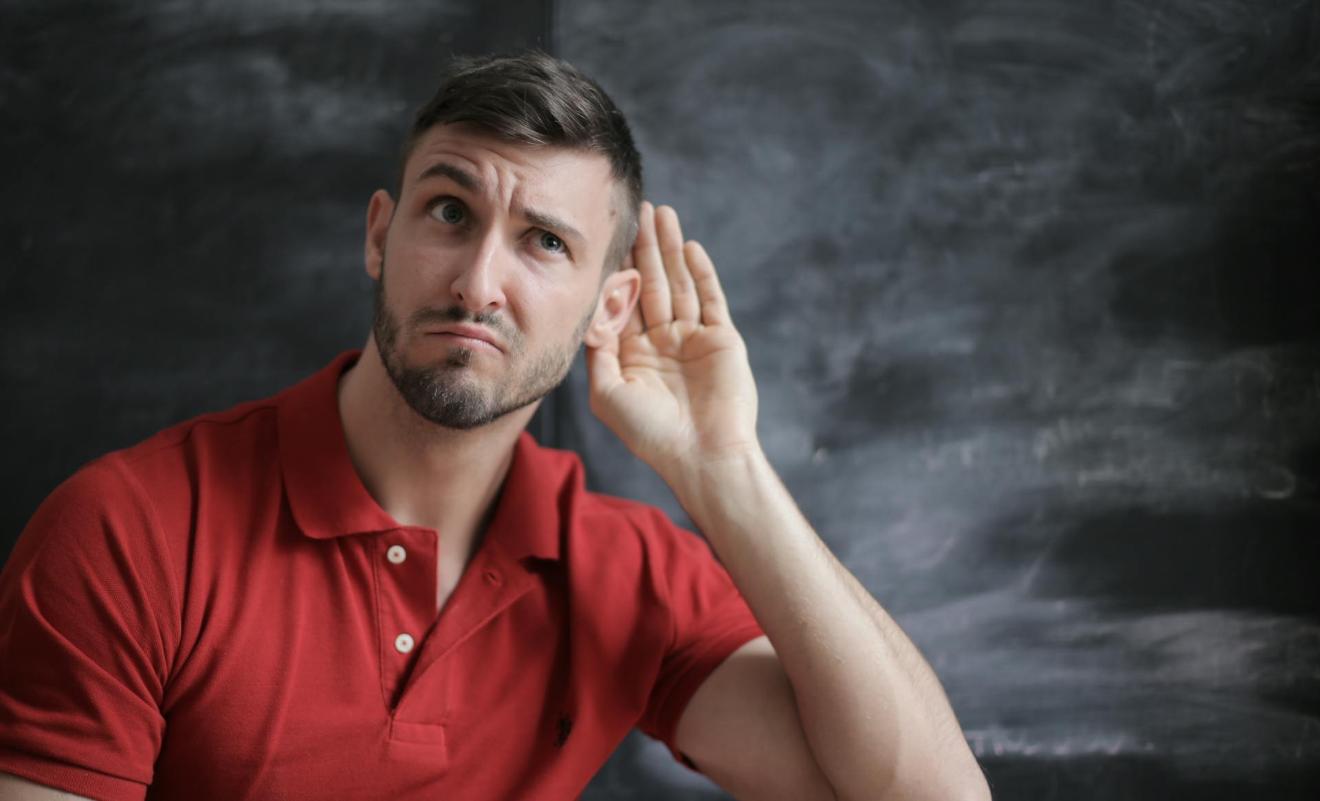 Un hombre ahuecando la oreja para escuchar | Fuente: Pexels