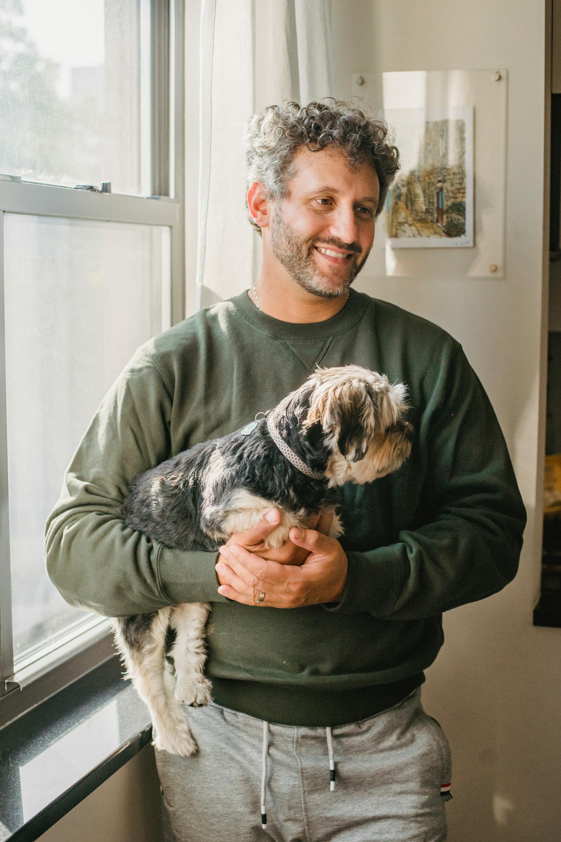 Un hombre con un perro en brazos cerca de una ventana | Fuente: Pexels