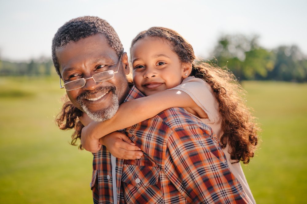 Nieta feliz abraza a su abuelo sonriente en el césped verde. | Fuente: Shutterstock