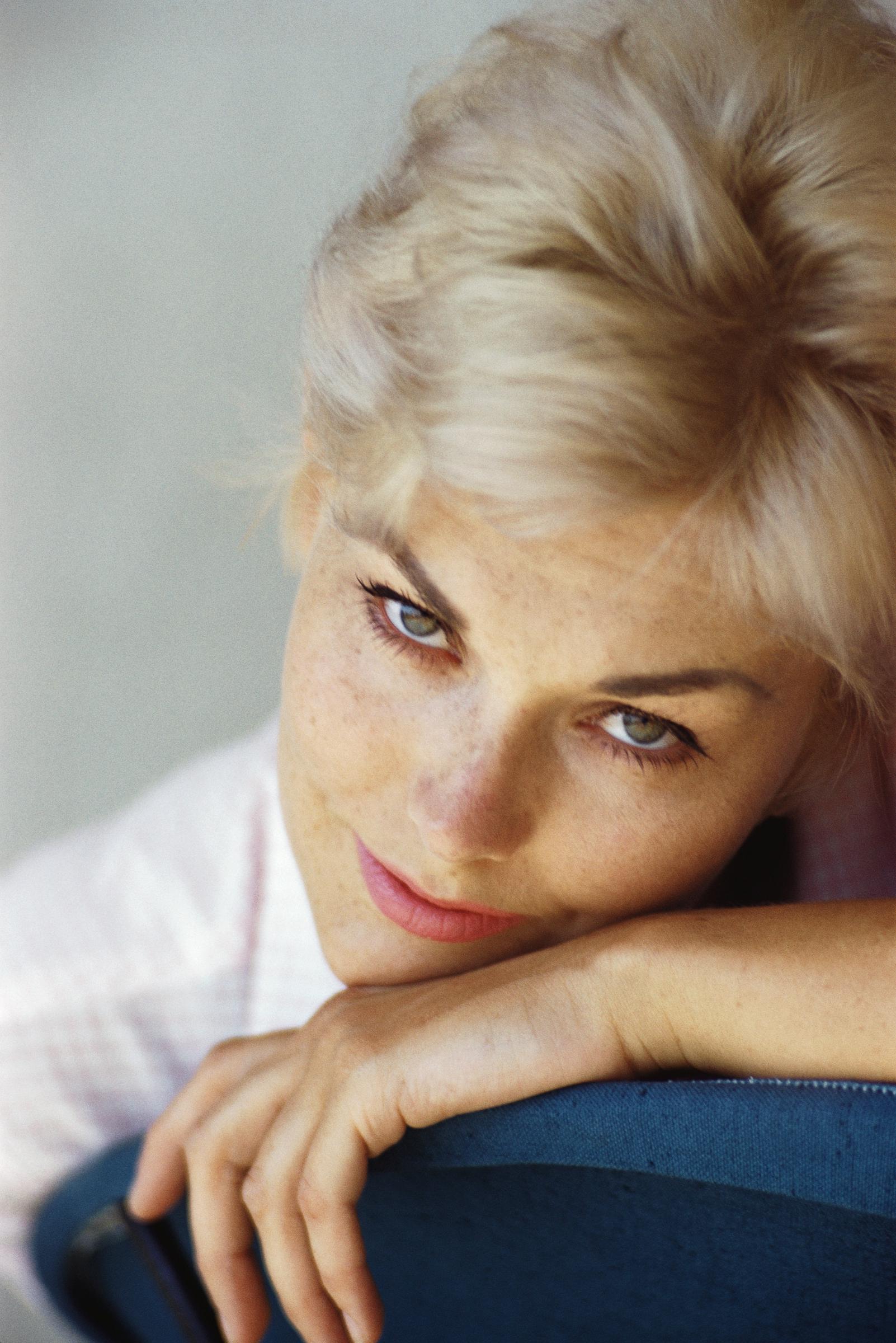 Kim Novak apoya la cabeza en el respaldo de una silla en un primer plano, con el pelo rubio peinado hacia atrás y la mirada fija en la cámara. | Fuente: Getty Images