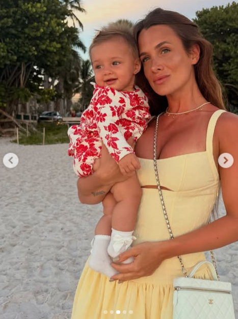 Camila Homs posó en la playa al atardecer sosteniendo en brazos a su pequeña hija Aitana. La modelo lució un vestido veraniego en tono amarillo pastel con escote cuadrado y abertura sutil bajo el busto, complementado con una cartera Chanel acolchada en color claro colgada al hombro. Por su parte, la bebé sonrió tiernamente luciendo un enterito estampado con flores rojas y medias blancas con lazos. | Fuente: Instagram/camihoms