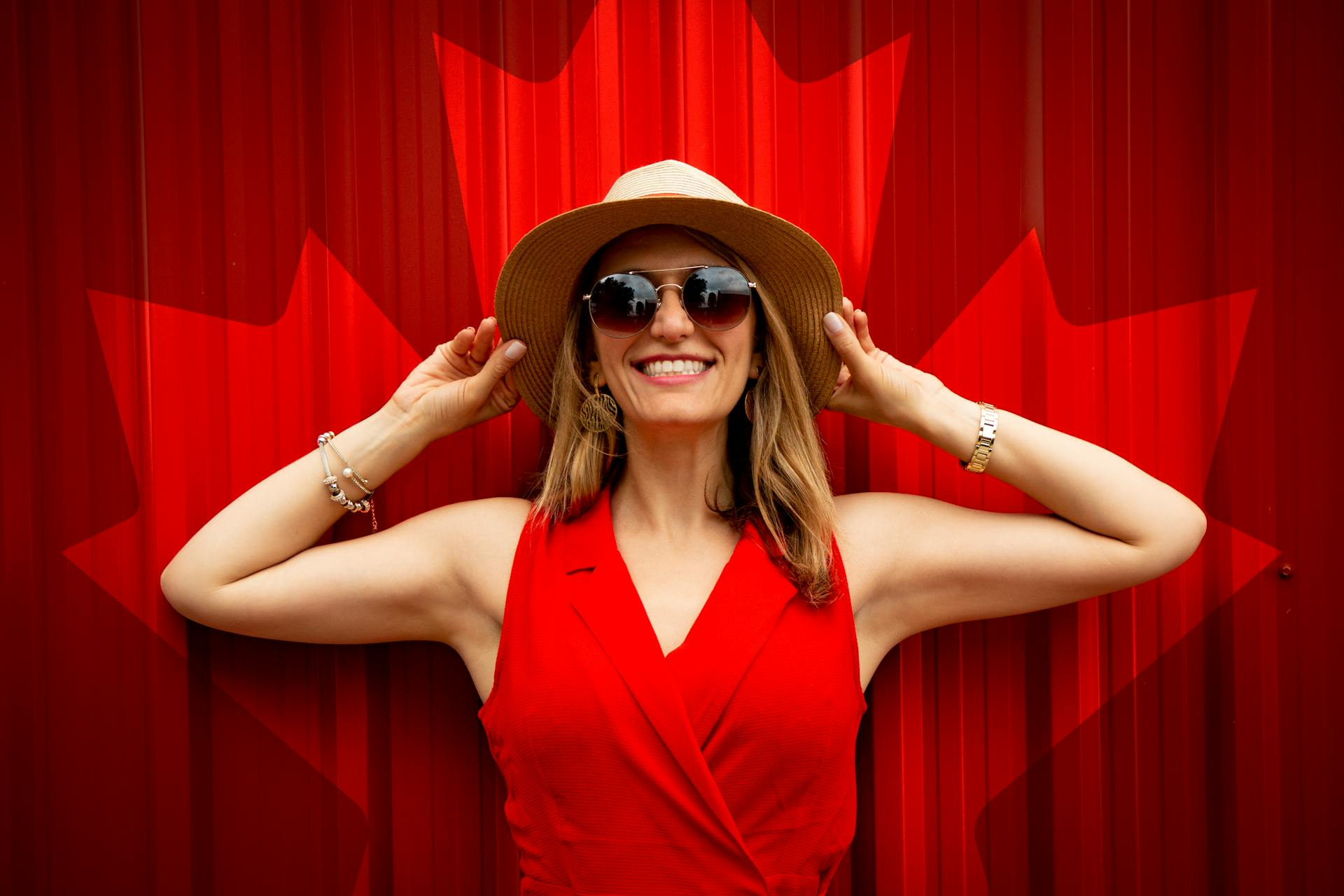 Una mujer sonriente con un vestido rojo, gafas de sol y sombrero sobre un fondo rojo | Fuente: Pexels