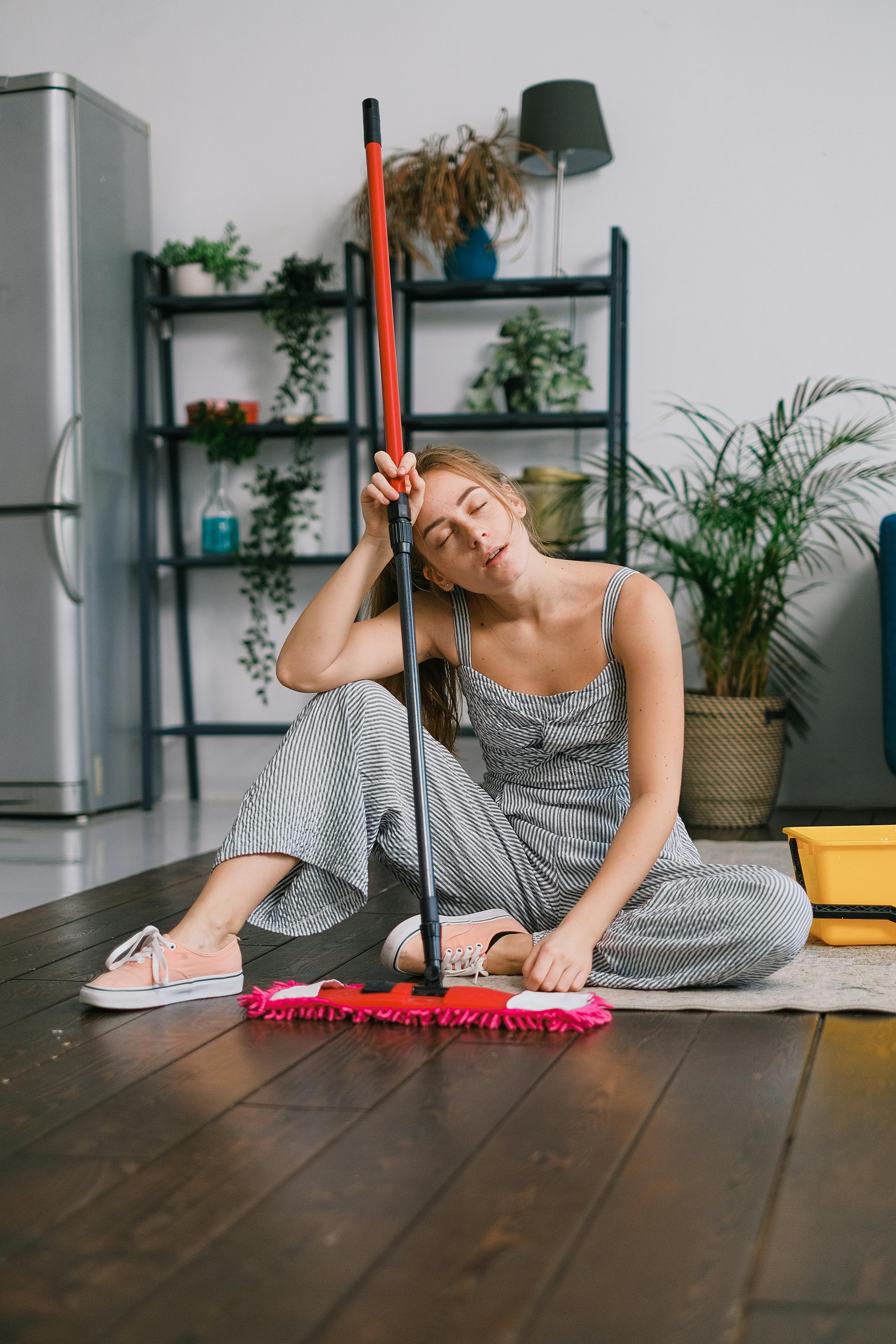 Mujer en el suelo con aspecto cansado mientras sostiene una mopa | Fuente: Pexels