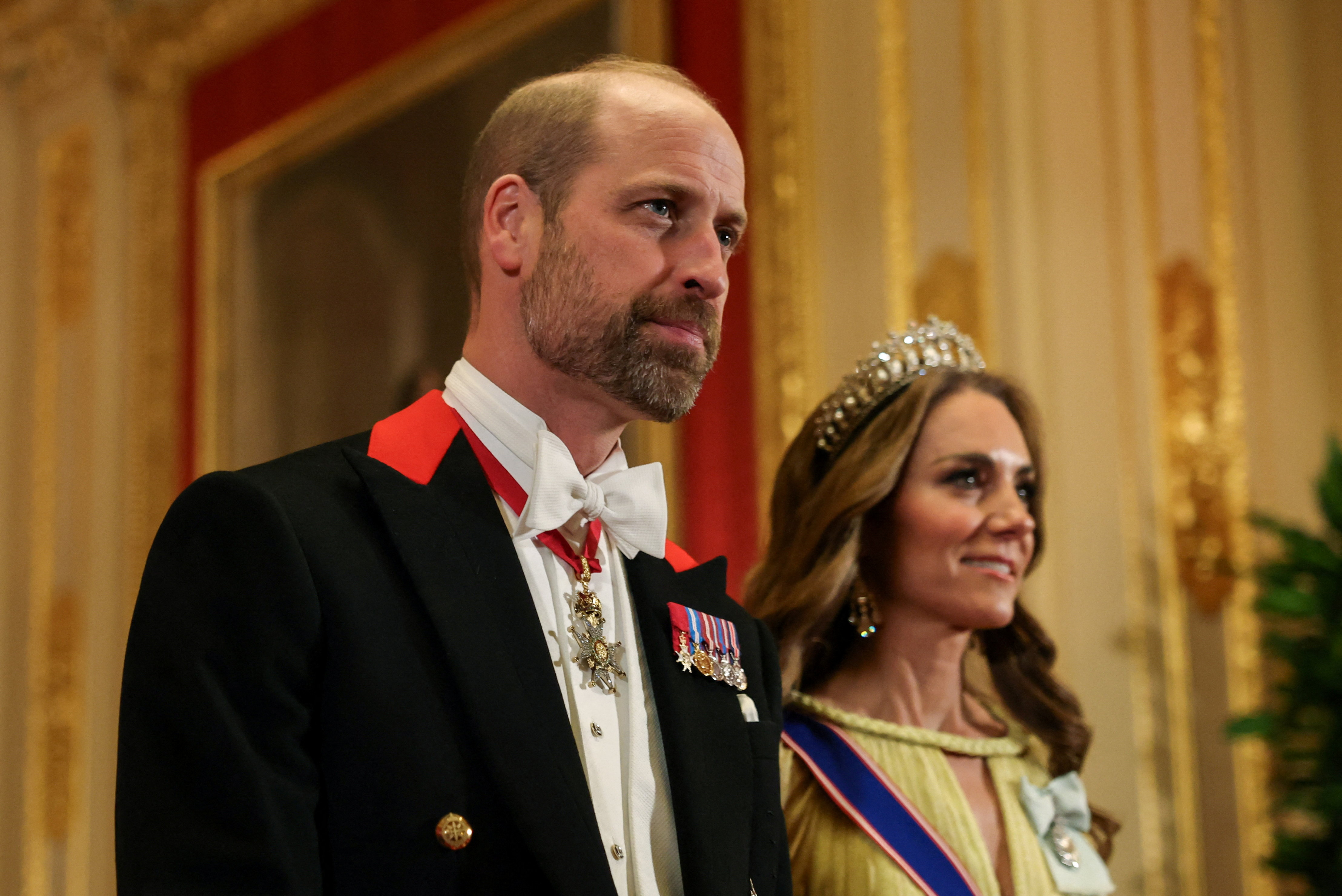 El príncipe William luce una barba corta junto a Catherine, princesa de Gales, durante su entrada nocturna al castillo de Windsor el 20 de octubre de 2026. El futuro rey viste frac negro tradicional de Windsor con detalles rojos en las solapas, corbata blanca y medallas en miniatura, mientras Catherine luce su tiara y vestido amarillo pastel. | Fuente: Getty Images