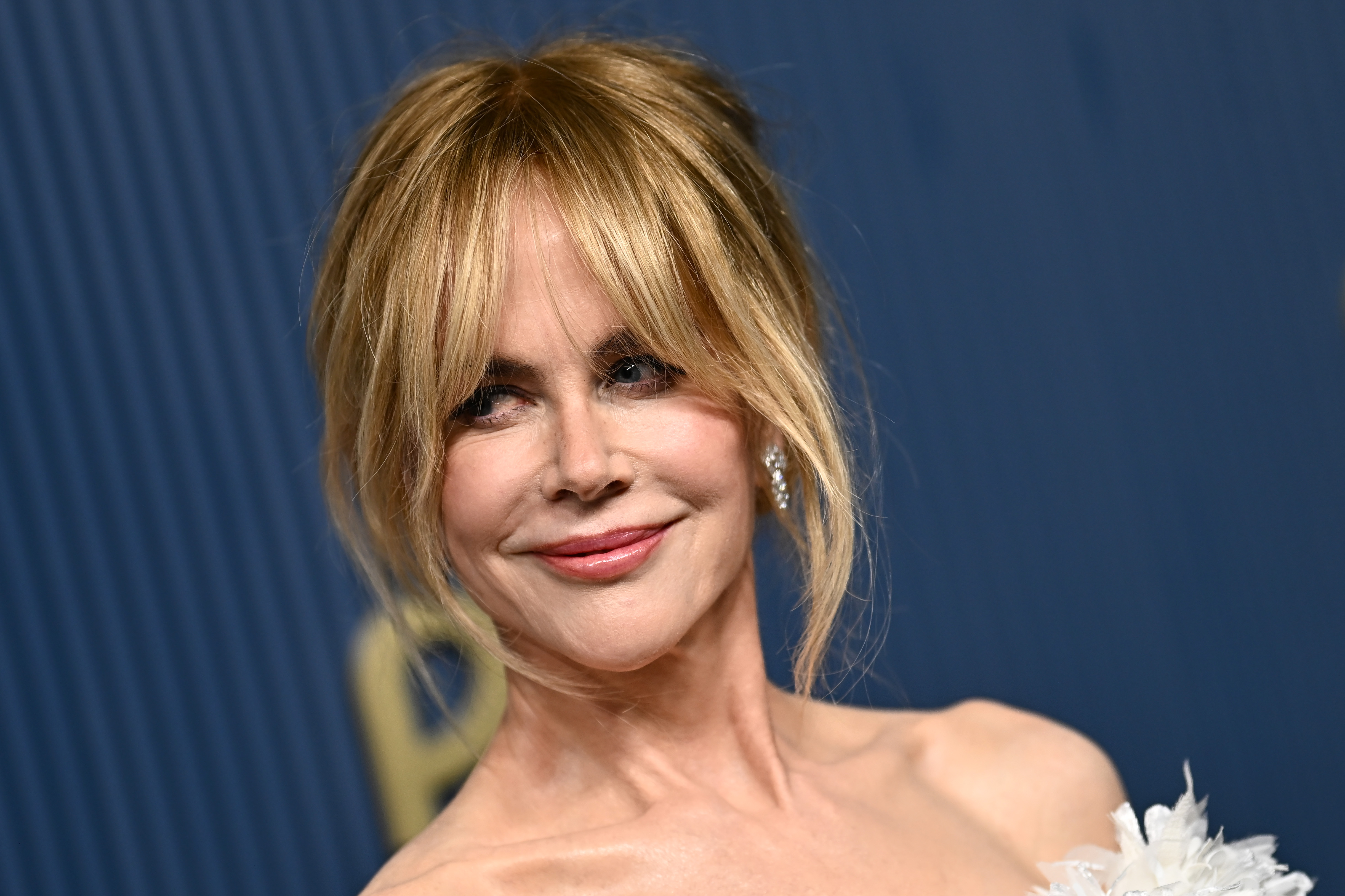 El retrato destaca el recogido suelto de Kidman, el flequillo que le enmarca el rostro y el suave tono rosa de sus labios, al tiempo que solo deja entrever parte del vestido. Su escote con plumas da una primera pista sobre el diseño antes de que se revele la silueta completa. | Fuente: Getty Images