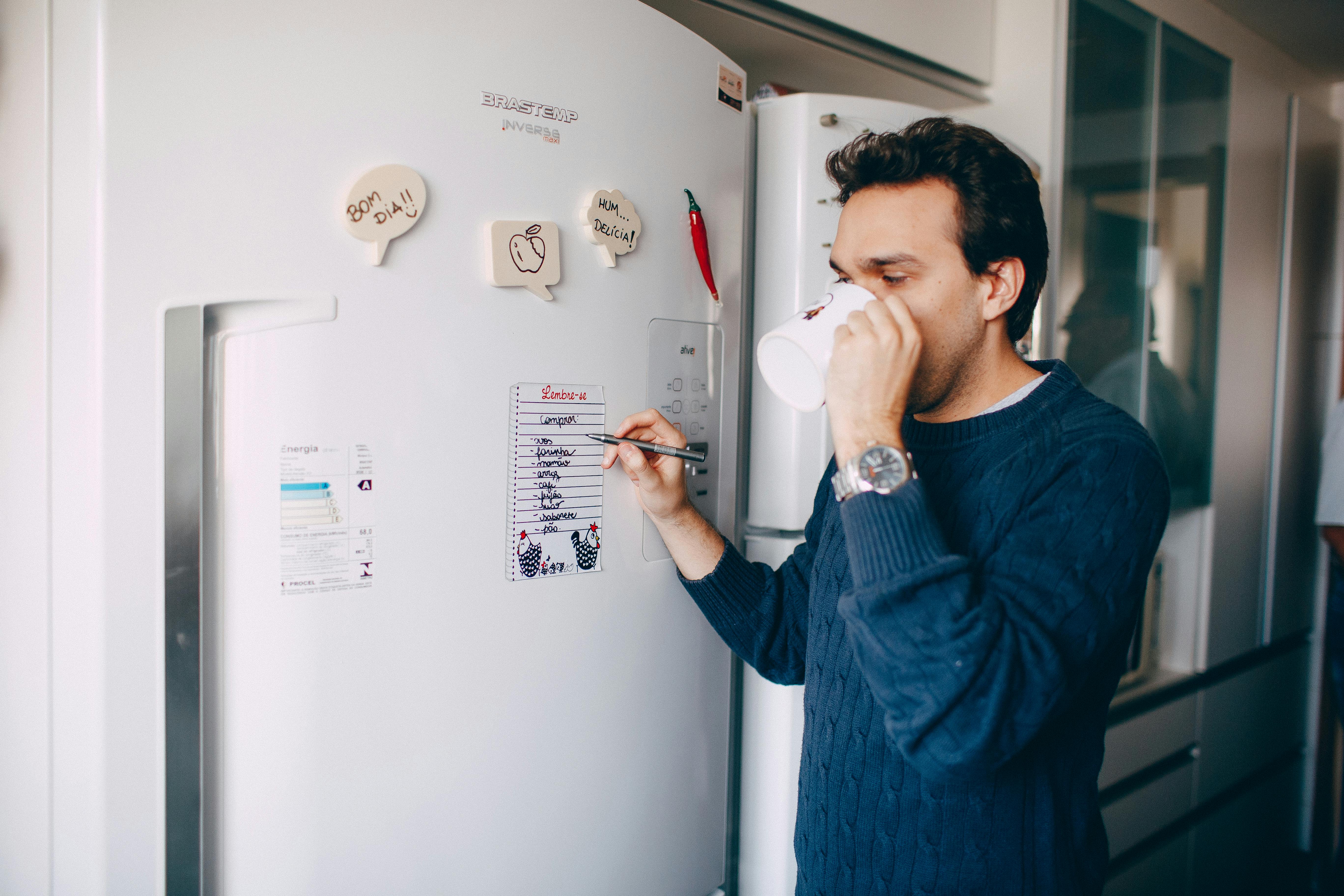 Hombre escribiendo una nota en una nevera | Fuente: Pexels