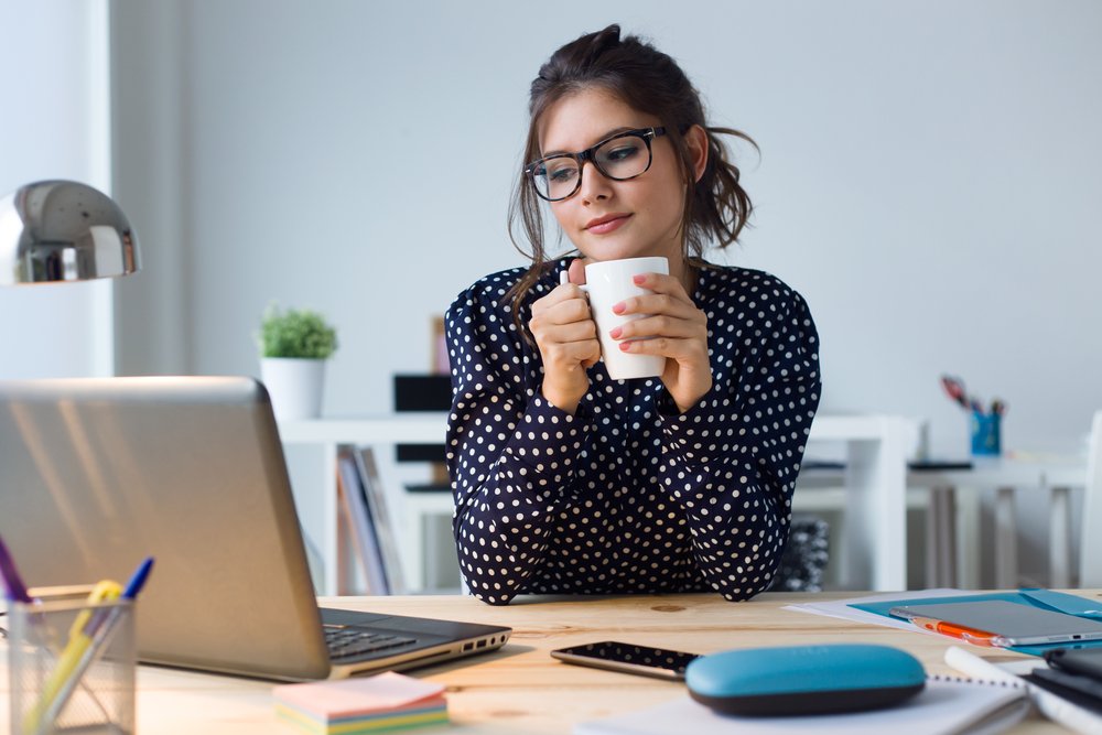 Mujer joven bebiendo café en su oficina. | Fuente: Shutterstock