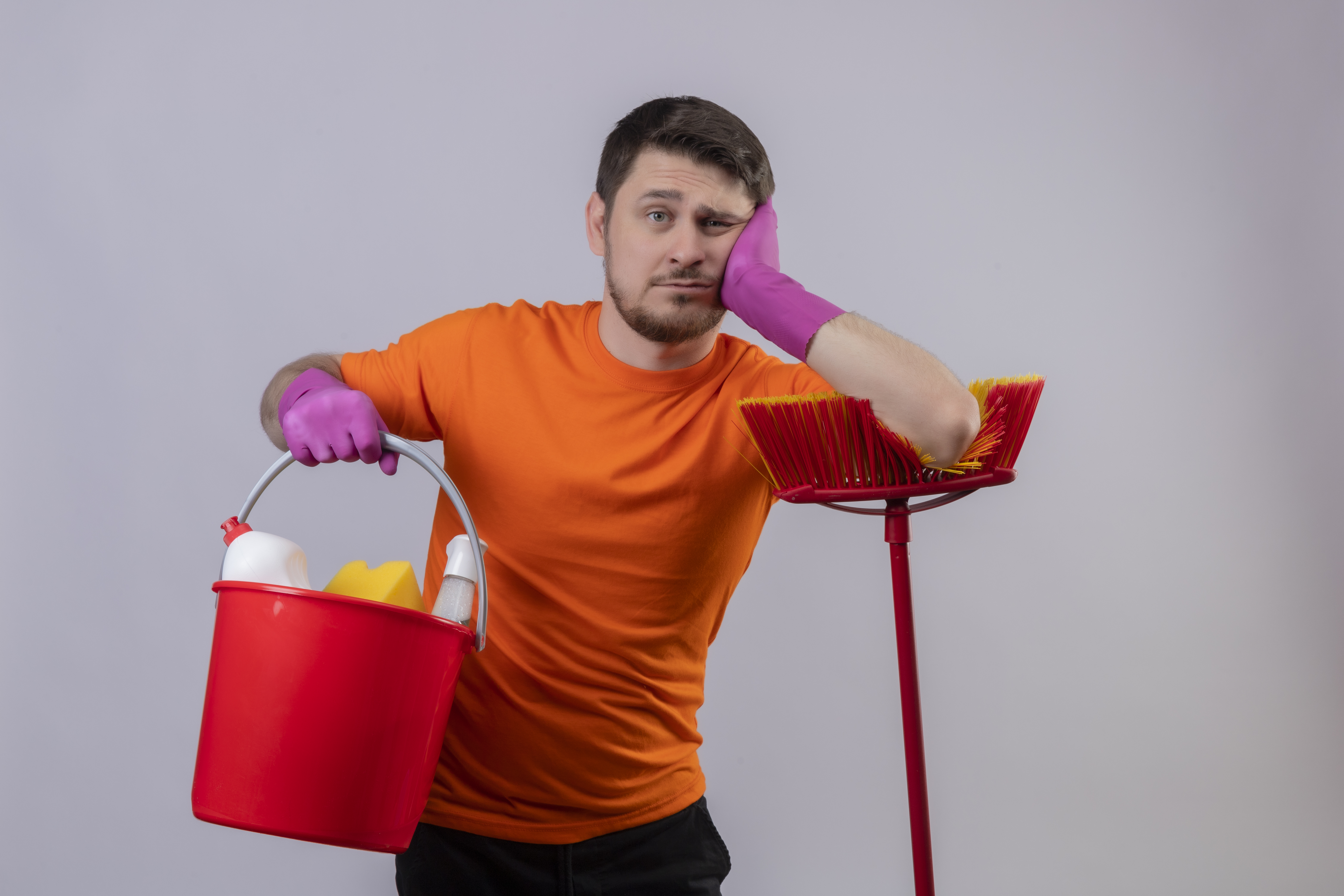 Joven vestido de naranja sujetando un cubo con utensilios de limpieza y apoyándose en una fregona | Fuente: stockking on Freepik