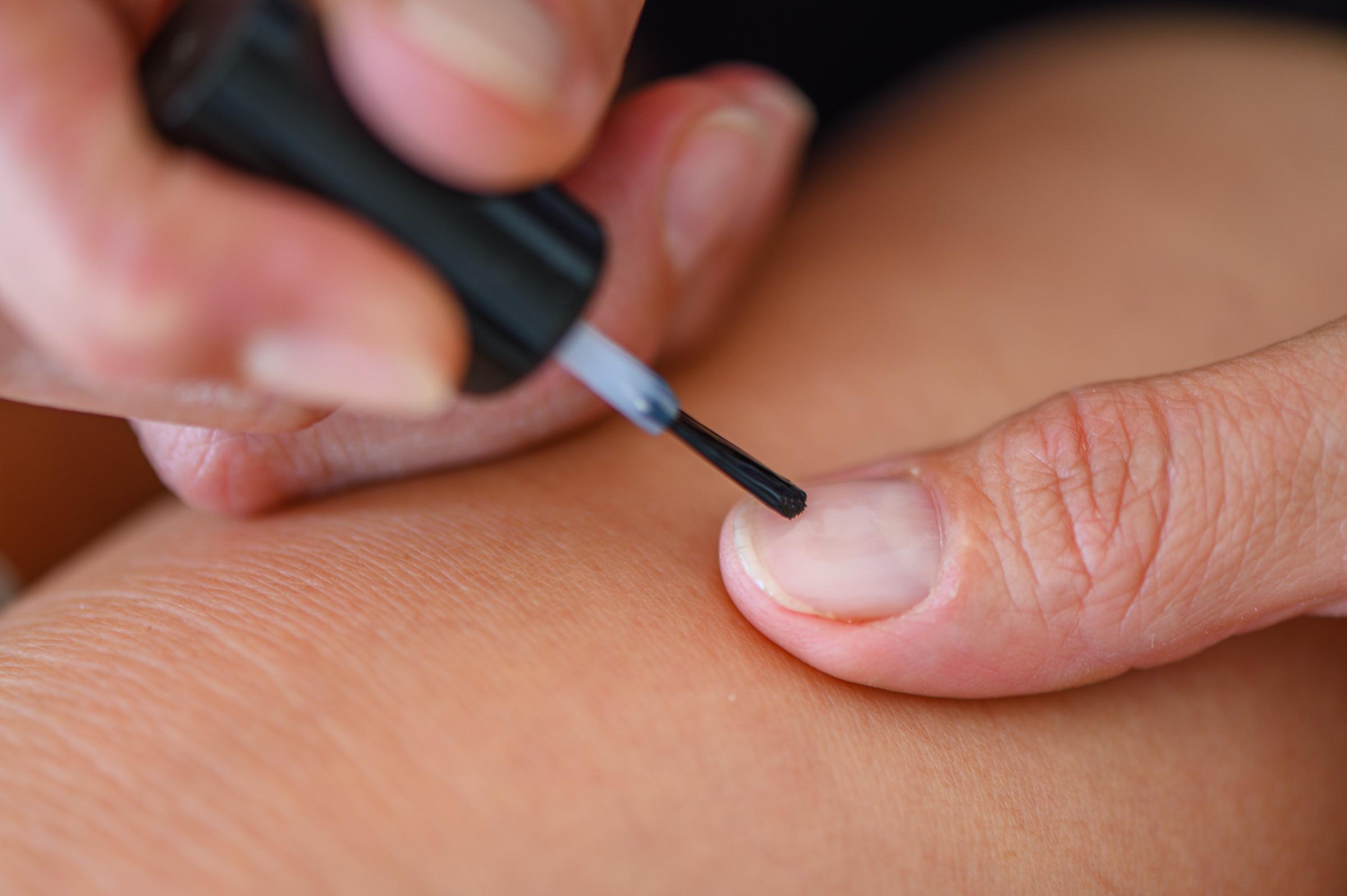 Mujer cubriéndose las uñas con barniz incoloro | Fuente: Shutterstock