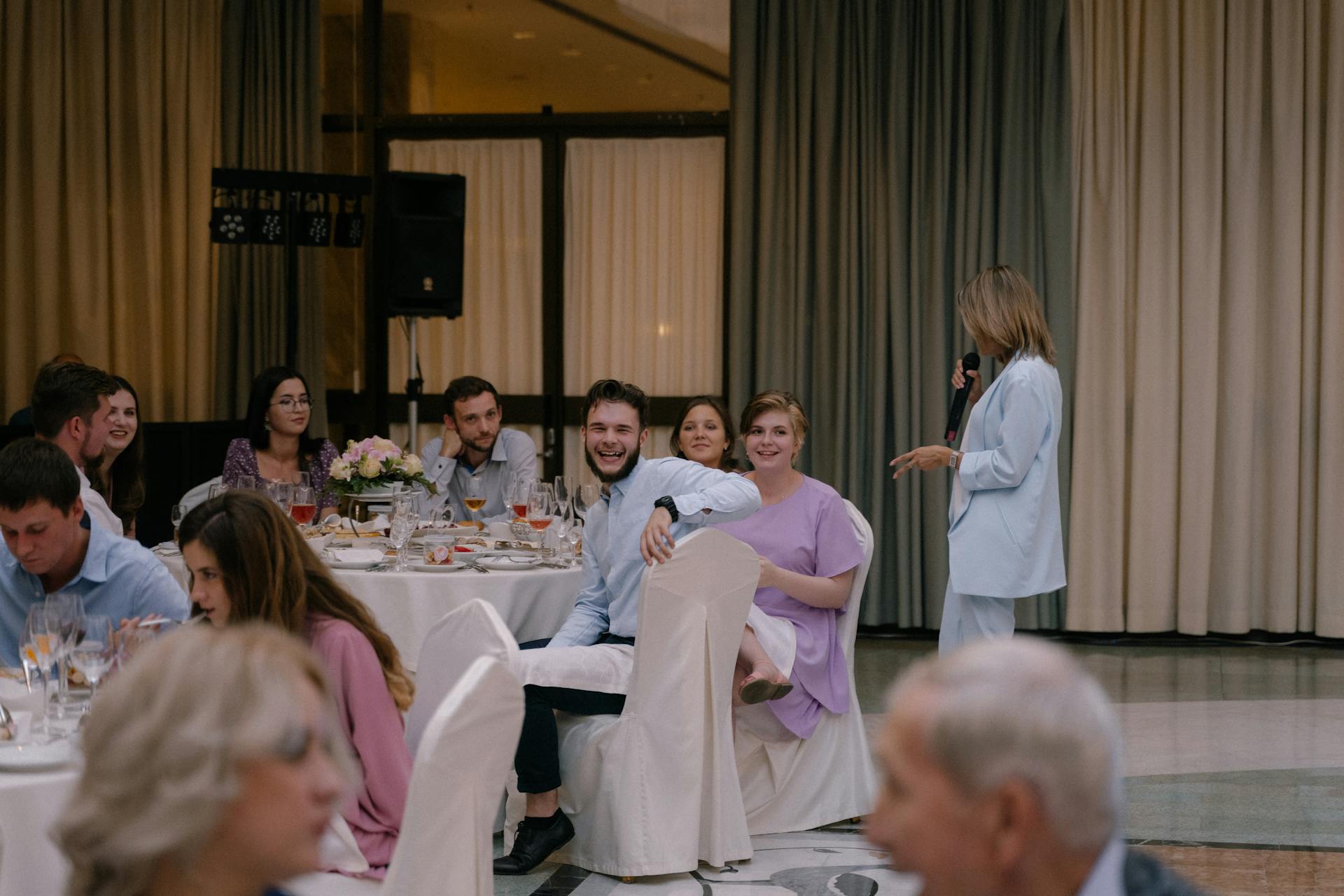 Invitados riendo mientras una mujer pronuncia un discurso al micrófono | Fuente: Pexels