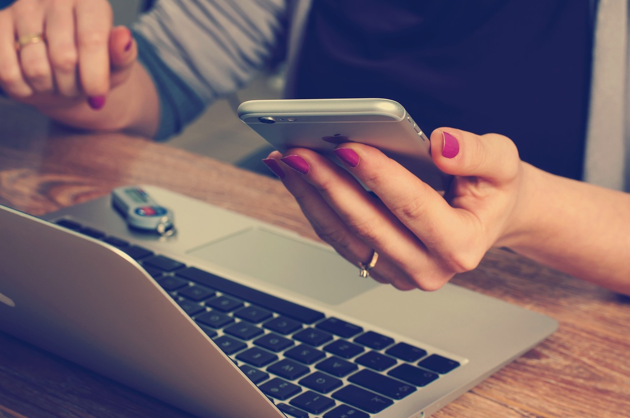 Una mujer sostiene un teléfono mientras trabaja en un portátil con un USB cerca | Fuente: Pixabay
