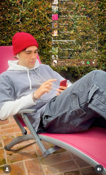 Ezequiel Laje (Leish) apareció recostado en una reposera fucsia navegando en su celular con auriculares puestos, luciendo un gorro de lana rojo, buzo gris y pantalón cargo negro. Sobre la imagen se proyectó una interfaz gráfica con una lista de reproducción que destacaba su nuevo sencillo "Placer Culposo". | Fuente: Instagram/leish.ar