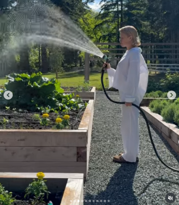 Vestida con un conjunto blanco de manga larga muy cómodo, Pamela Anderson riega los exuberantes parterres elevados con una manguera bajo el cálido sol de verano en Arcady. Rodeada de caléndulas amarillas, frondosas plantas de hoja verde y senderos de grava, disfruta de la belleza tangible de regenerar su jardín, y acompaña la foto con este mensaje: "Pienso en la vida como un jardín… Puedes volver a plantar, empezar de nuevo y hacerla tuya. 🤍 Con cariño, P". | Fuente: Instagram/pamelaanderson
