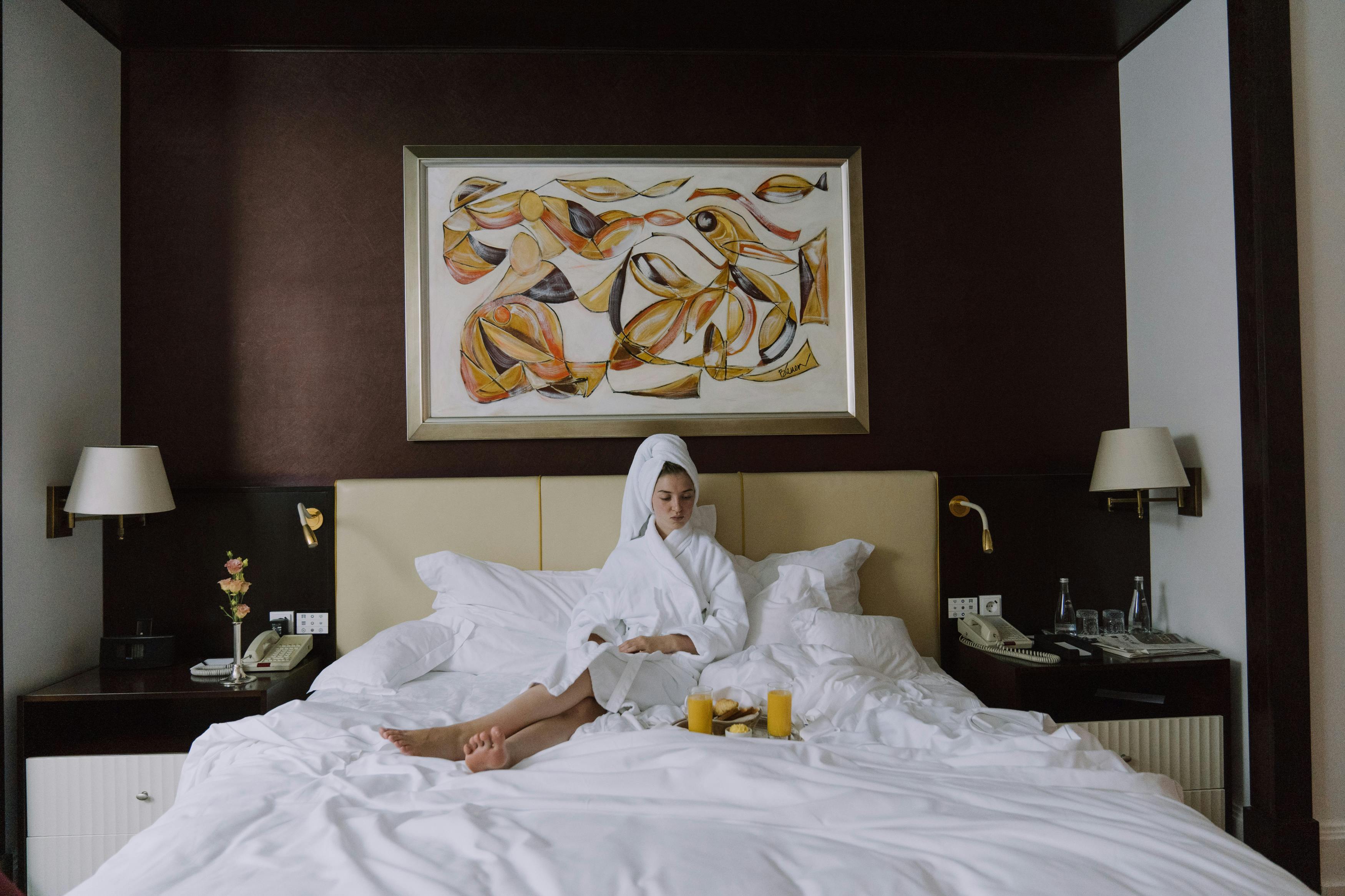 Una mujer alterada sentada en la cama de una habitación de hotel en albornoz | Fuente: Pexels