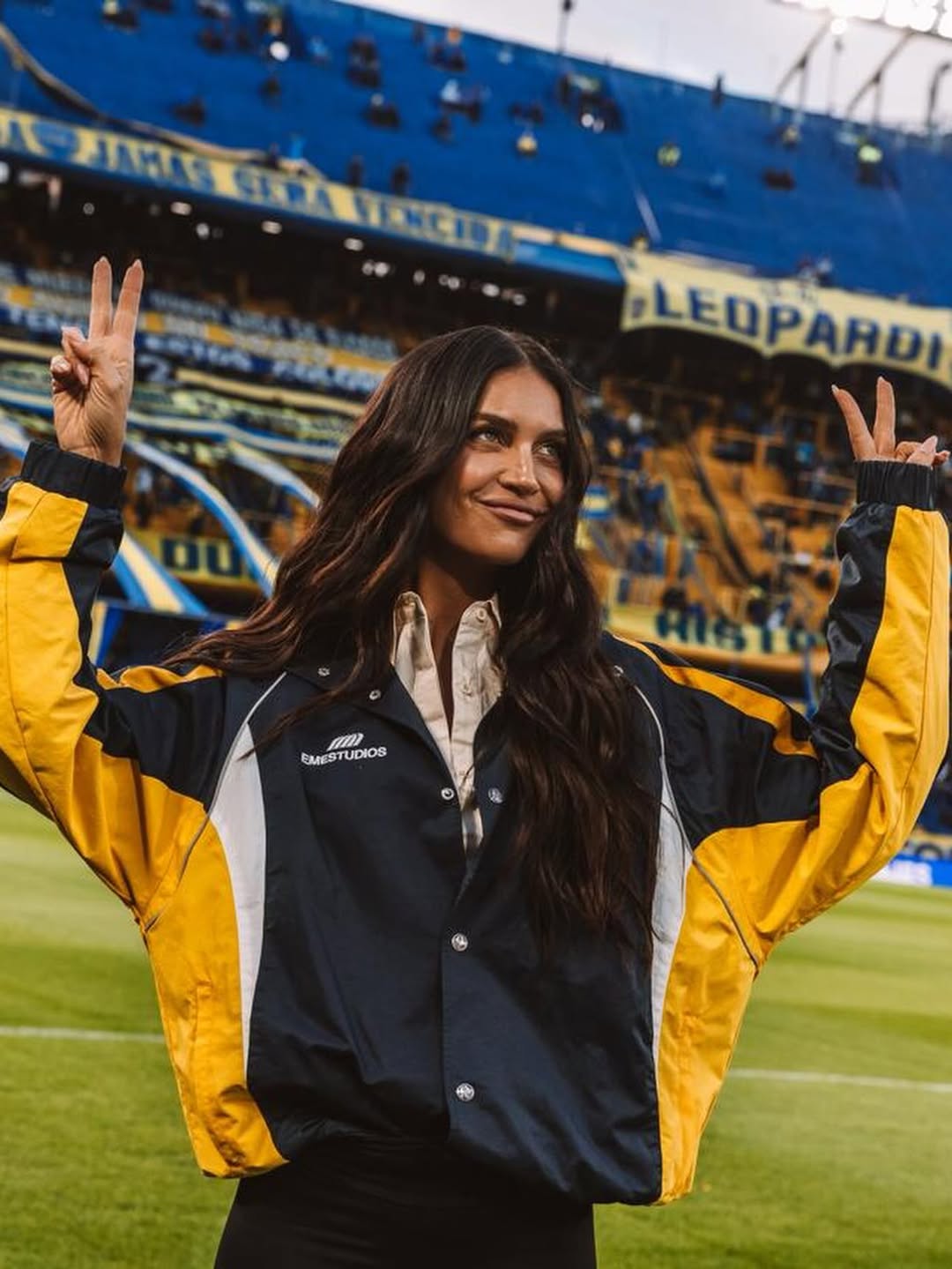 Zaira Nara levanta las manos mientras posa sobre el césped de La Bombonera con un look en los colores de Boca Juniors. | Fuente: Instagram/zaira.nara