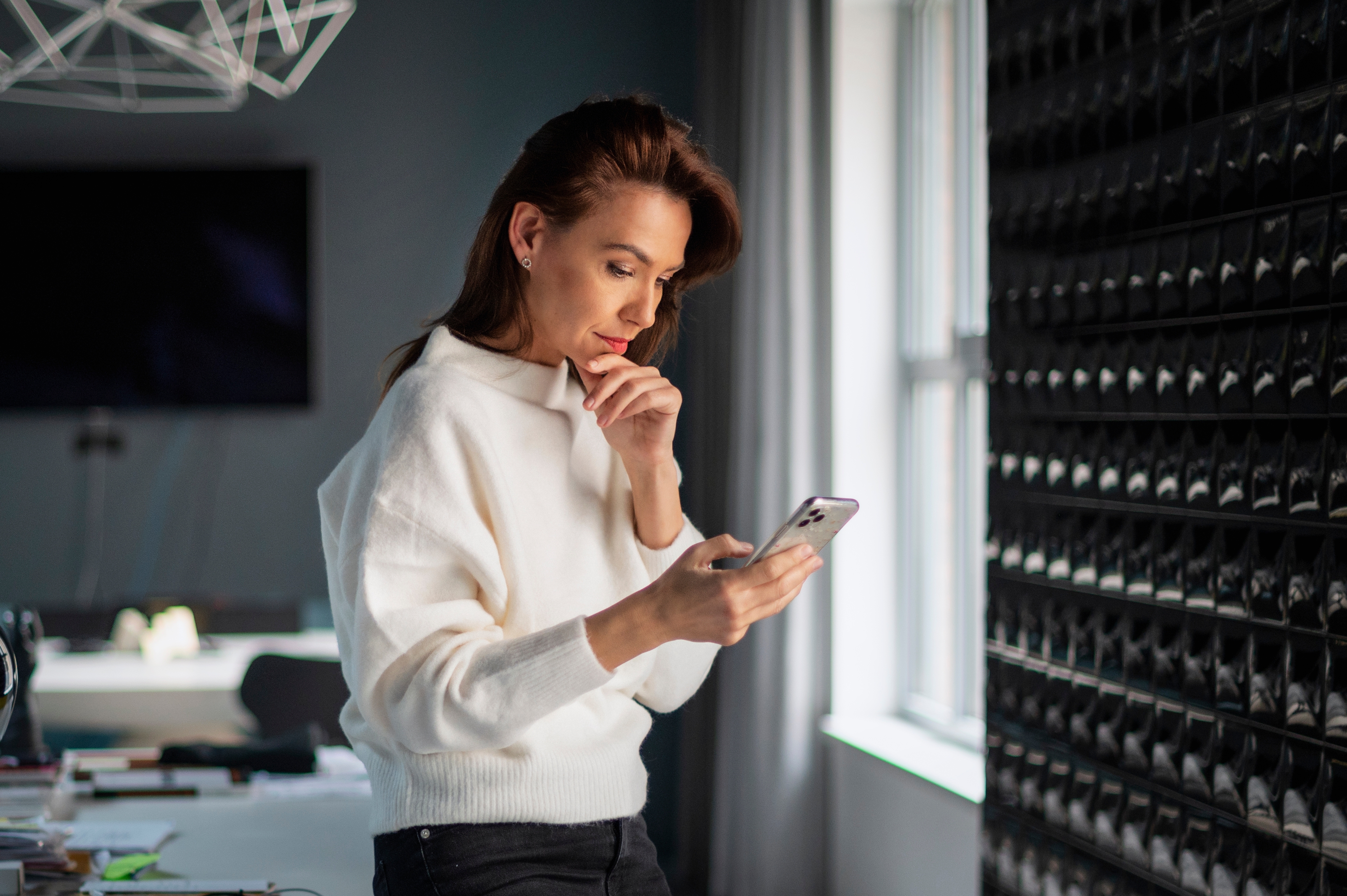 Una mujer de negocios de mediana edad de pie en la oficina y utilizando un smartphone. | Fuente: Shutterstock