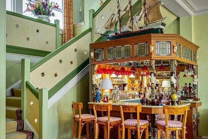 Una maqueta de velero corona una elaborada barra empotrada situada junto a la escalera, lo que le da un toque náutico a esta histórica casa de la isla. | Fuente: Facebook/LegacySIR