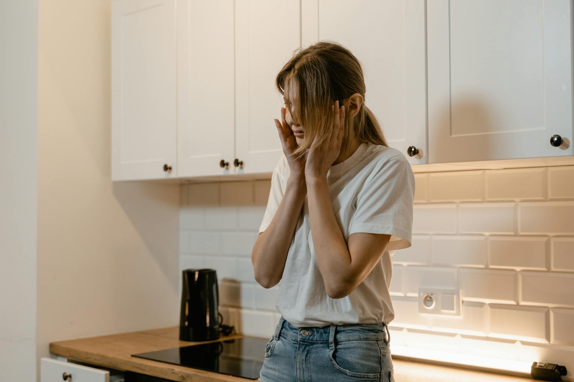Una mujer en una cocina ahuecándose la cara con las manos | Fuente: Pexels