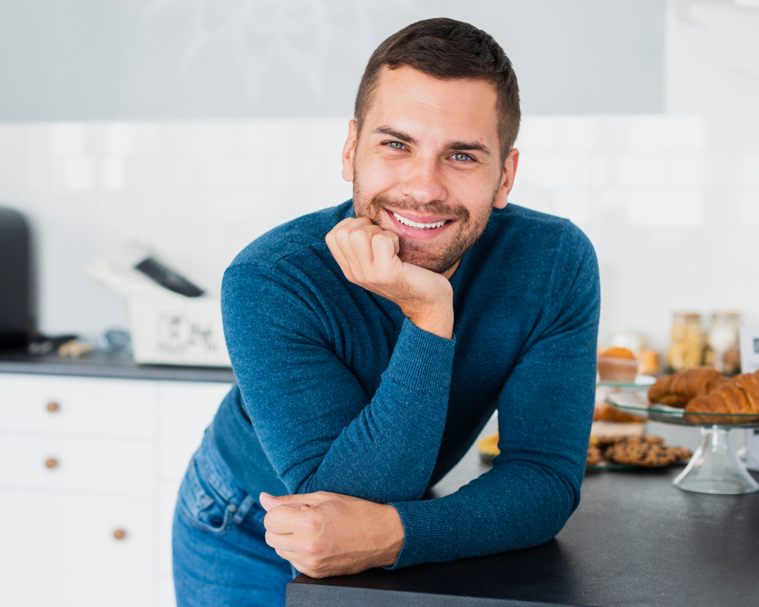 Un hombre apoyado en la encimera de la cocina y sonriendo | Fuente: Freepik