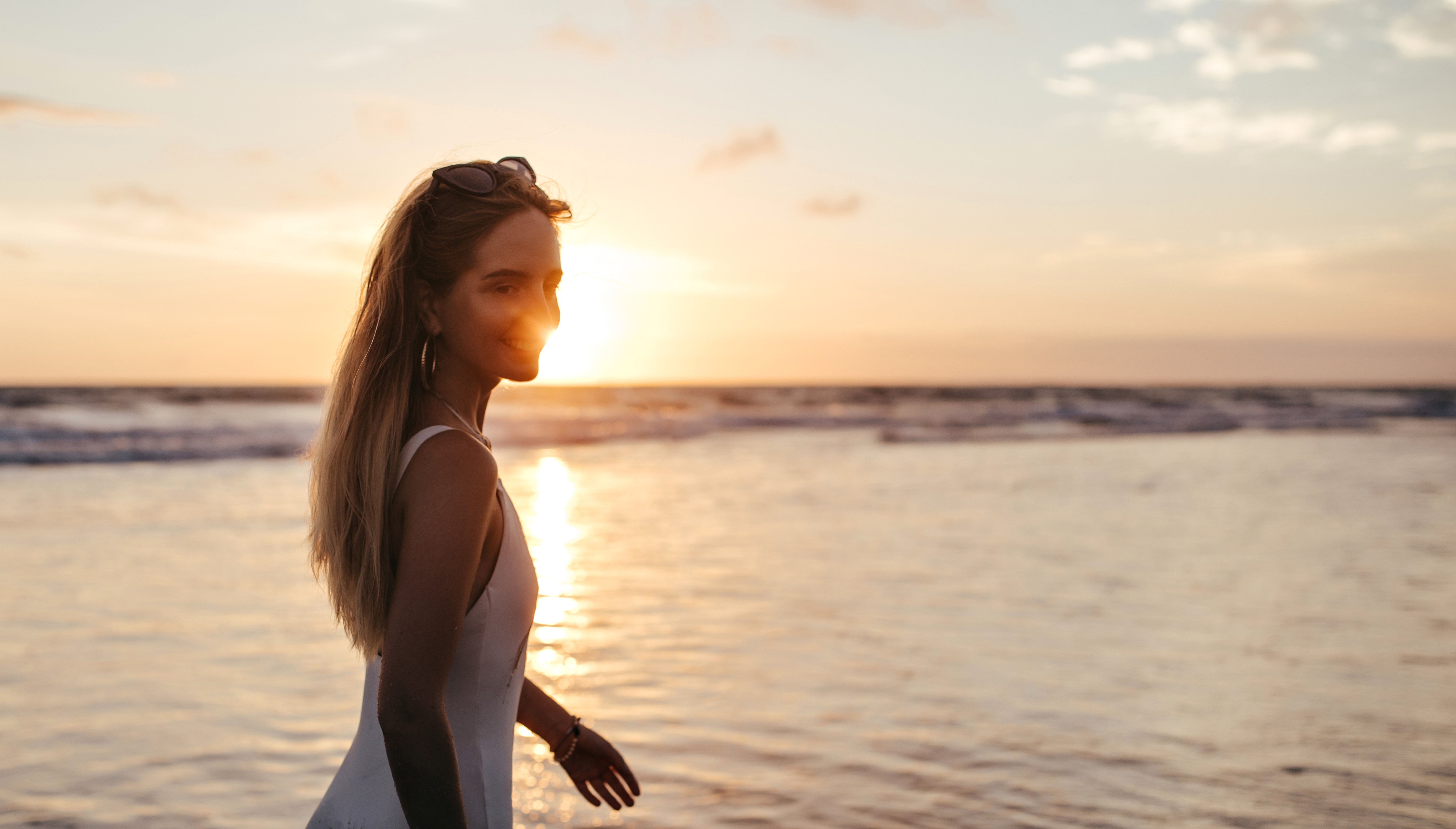 Una mujer sonriente en bañador blanco cerca del mar | Fuente: Freepik