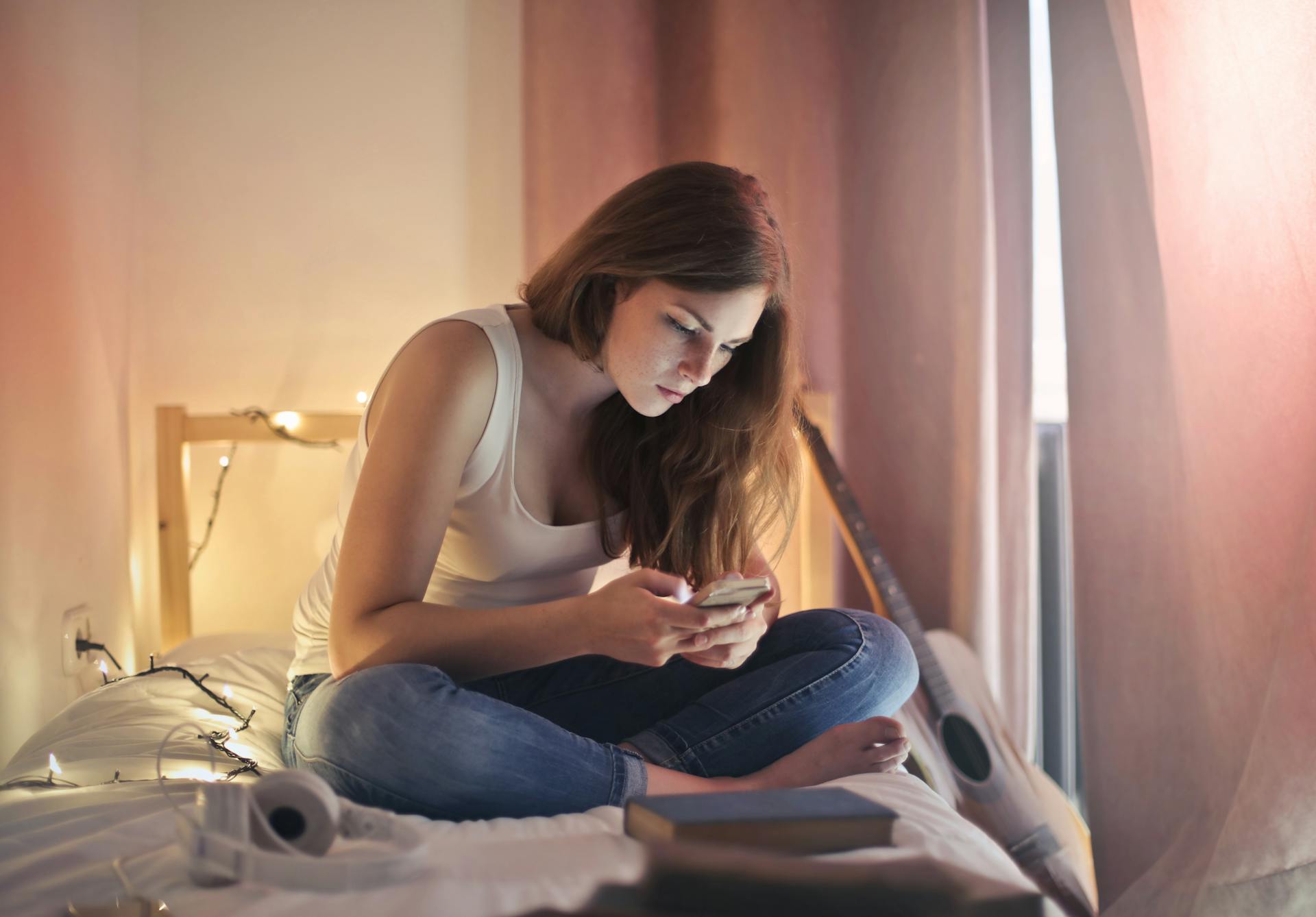 Una mujer usando su teléfono mientras está sentada en su cama | Fuente: Pexels