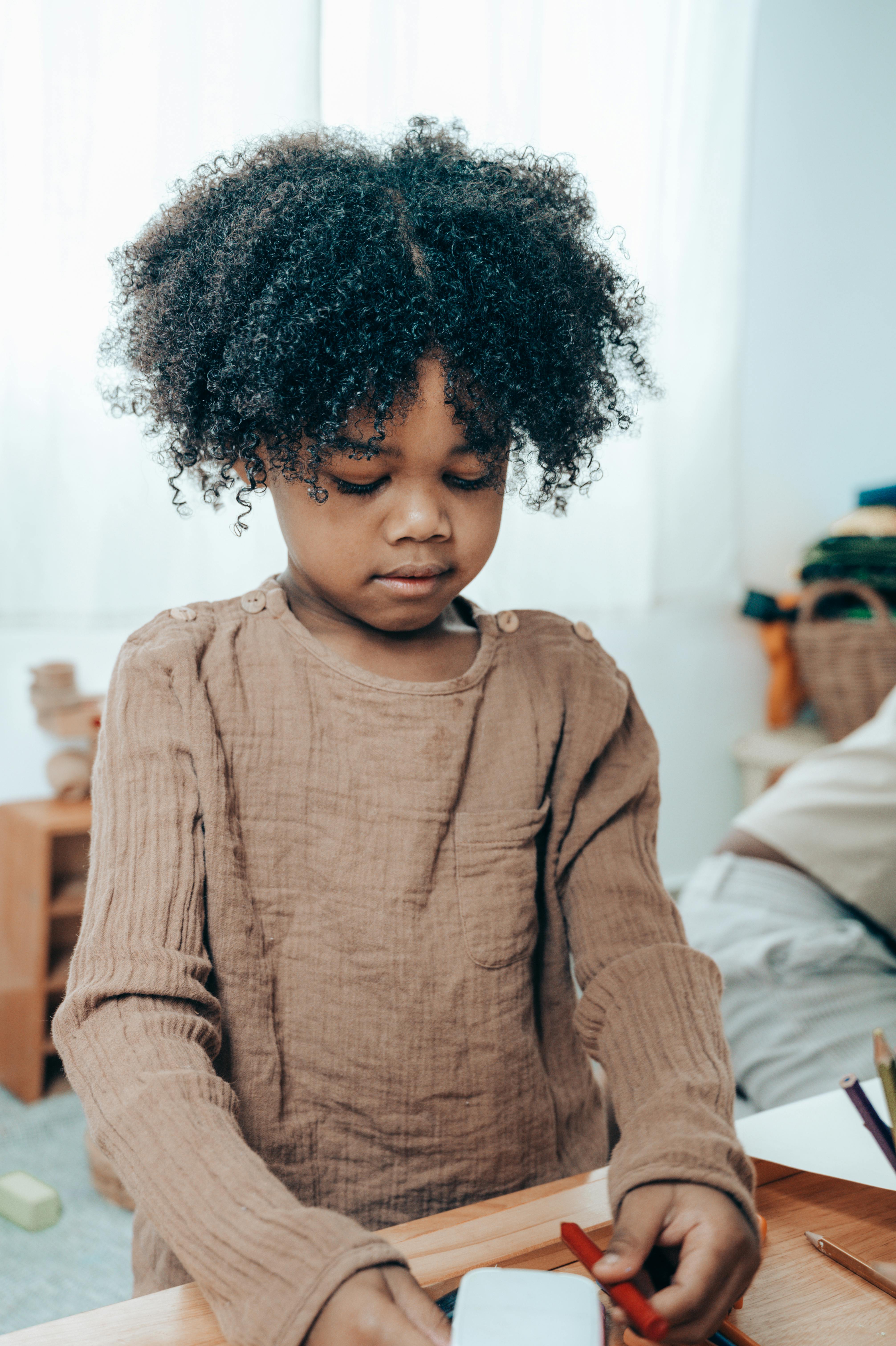 Una niña mirando un papel y un lápiz de color | Fuente: Pexels