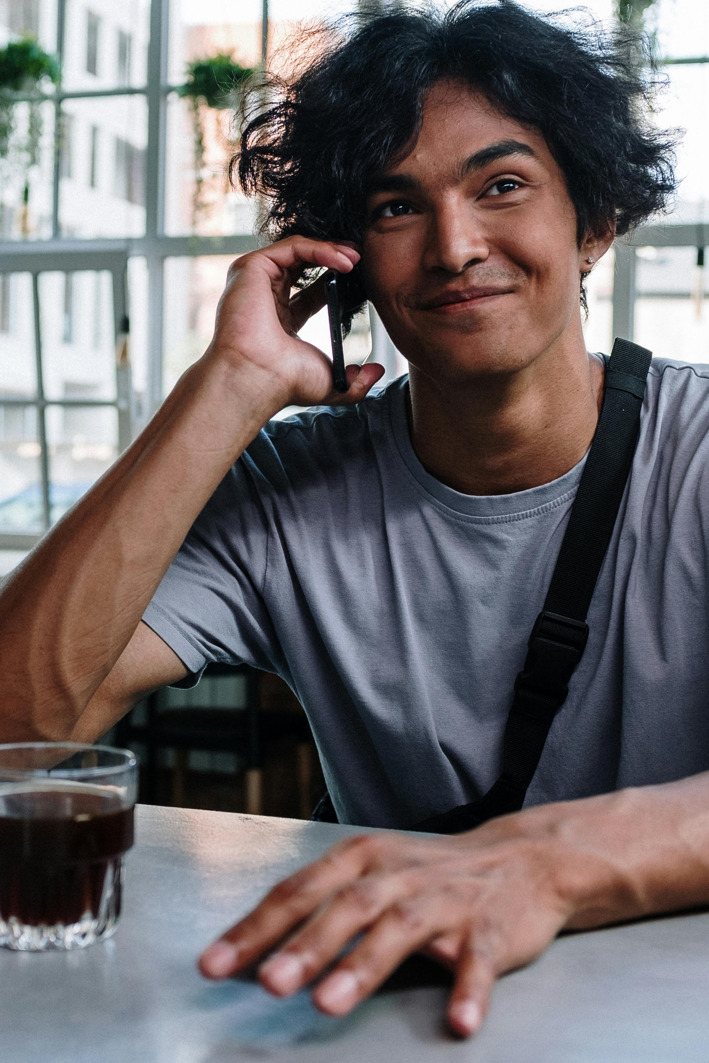 Un hombre feliz hablando por teléfono mientras toma una copa | Fuente: Pexels