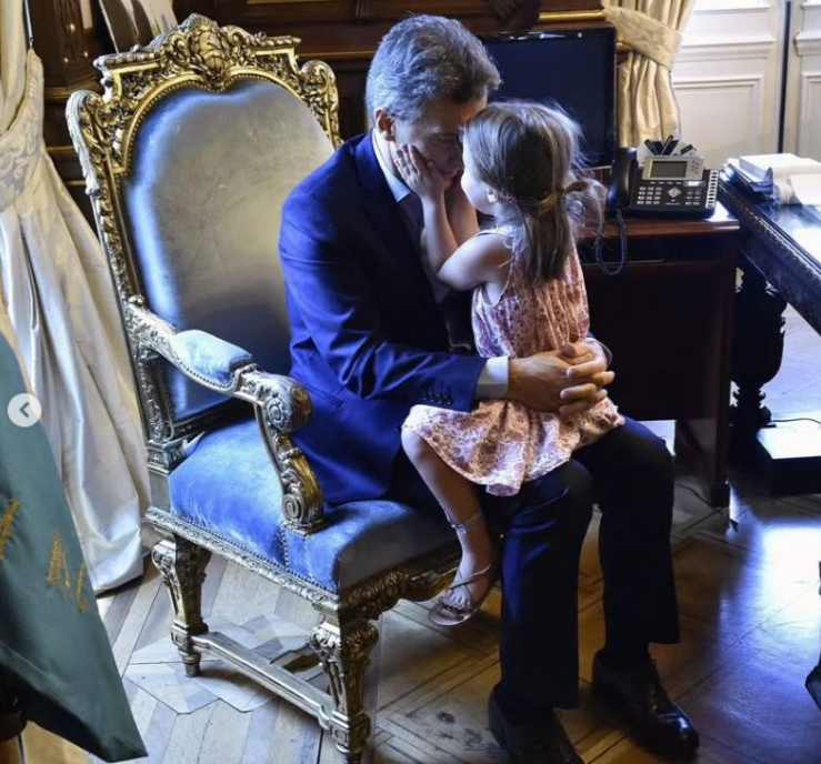 Mauricio Macri y su hija Antonia comparten un tierno momento en el despacho presidencial. Sentada sobre su regazo en un sillón clásico de terciopelo azul y dorado, la pequeña, vestida con un solero floreado y sandalias, apoya sus manos en el rostro de su padre mientras él la abraza con afecto. | Fuente: Instagram/mauriciomacri